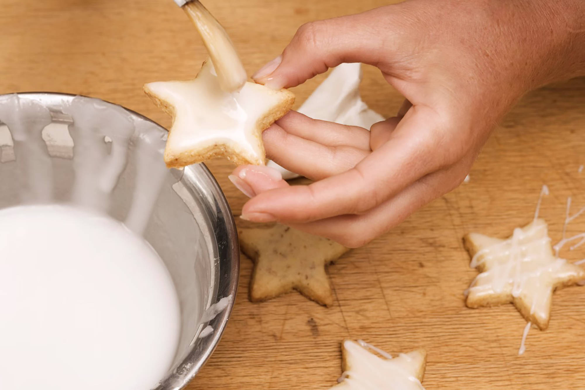 Plätzchen in Form von Sternen werden mit einer Glasur bestrichen.
