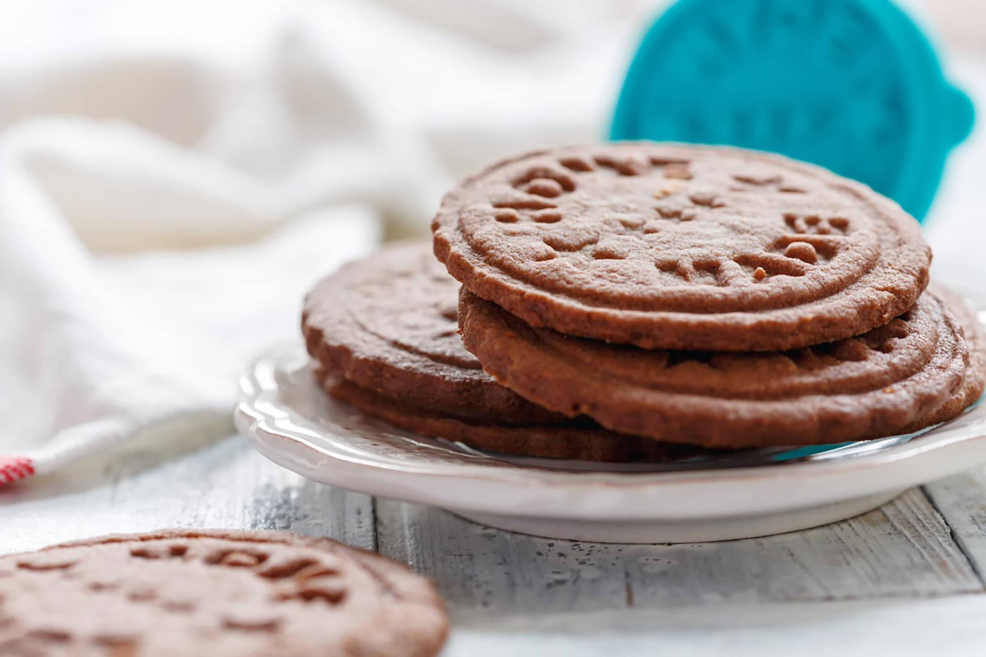 Geprägte Schokoladenplätzchen auf weißem Teller, mit einem blauen Keksstempel im Hintergrund.
