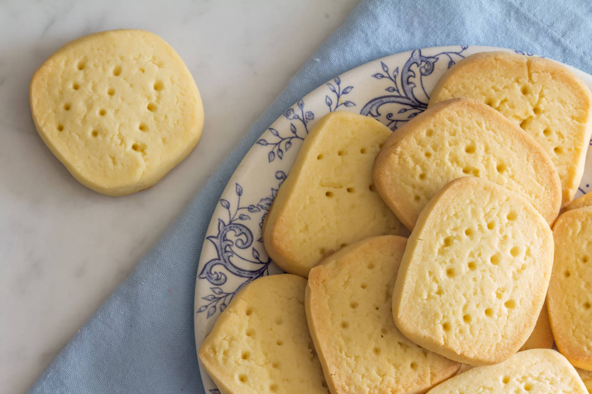 Auf einem Teller liegt Shortbread und neben dem Teller liegt ein einzelnes Shortbread auf dem Tisch.