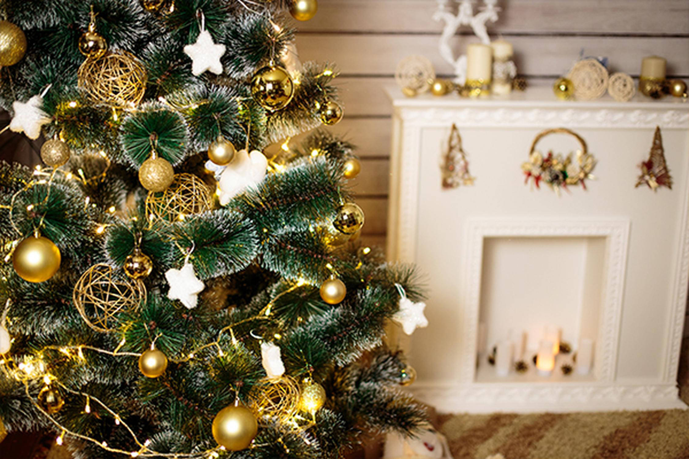 Christbaum mit goldenem und weißem Schmuck vor einem weißen Kamin