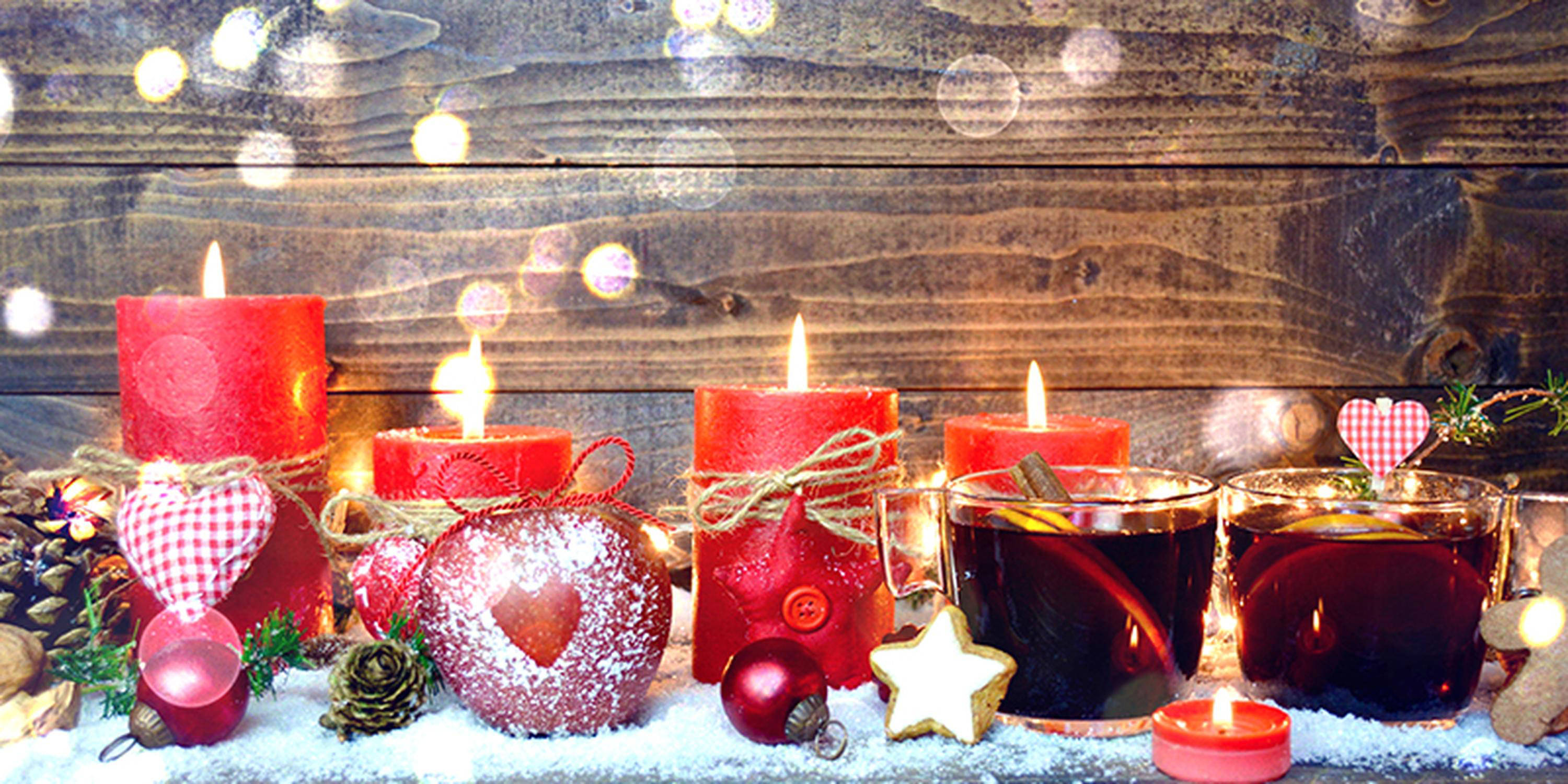 Vier unterschiedlich hohe, rote Kerzen brennen. Davor stehen Plätzchen und Glühwein