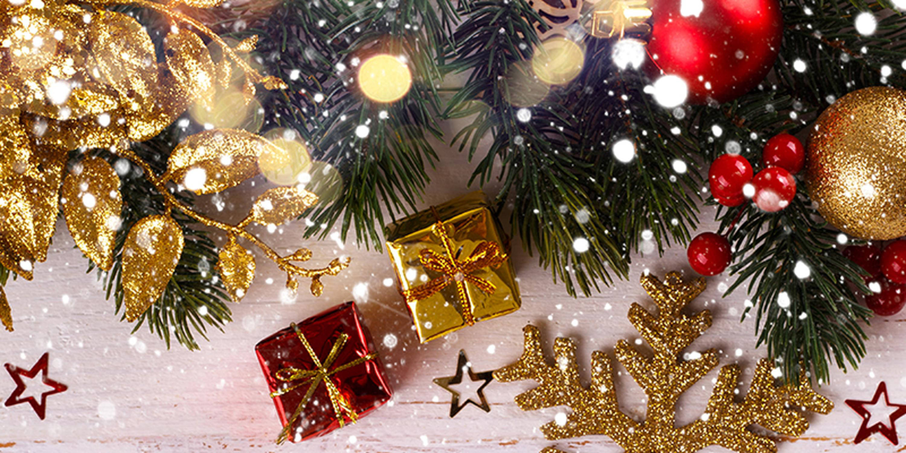 Tannenzweige geschmückt mit goldener und roter Weihnachtsdekoration aus Kugeln und Geschenkpäckchen. Es schneit.
