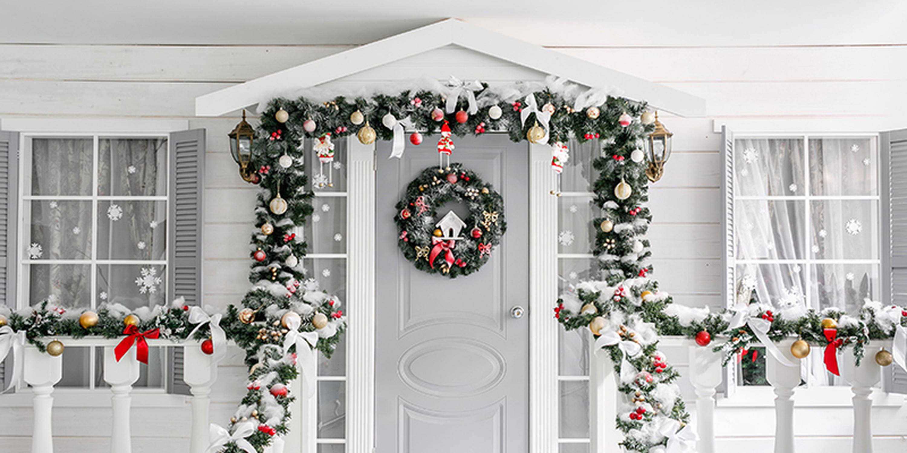Klassische Weihnachtsdekoration mit Tannenzweigen, Christbaumschmuck und Adventkranz an einer weiß-grauen Haustür
