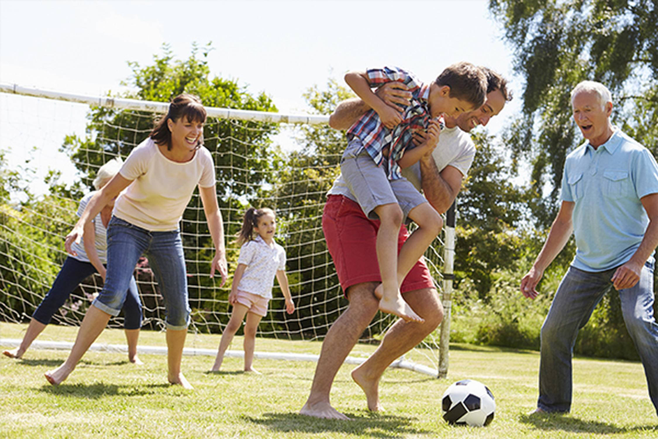 Zwei Männer, zwei Frauen und zwei Kinder spielen Fußball auf einer grünen Wiese