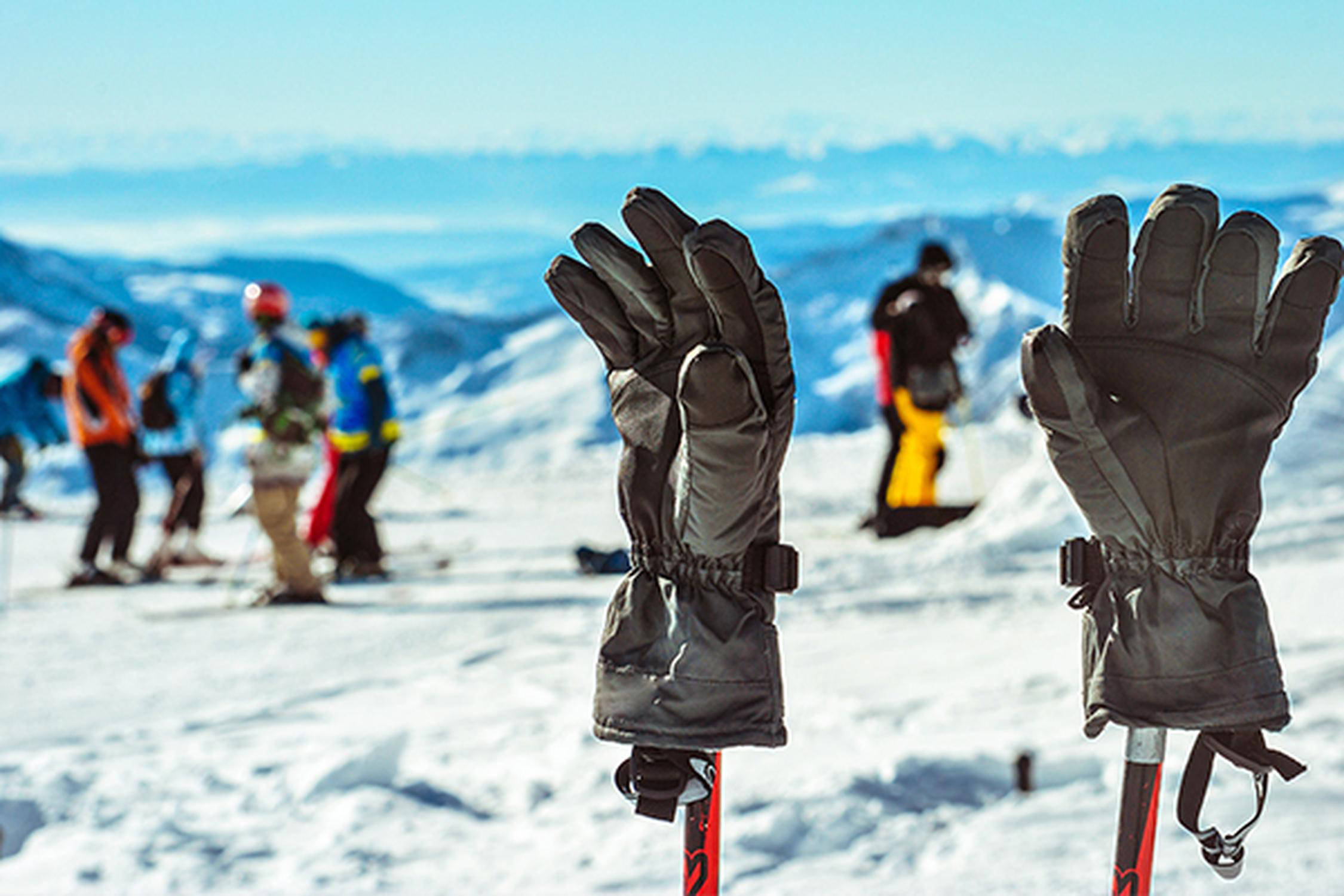 Zwei schwarze Skihandschuhe stecken auf zwei roten Skistöcken