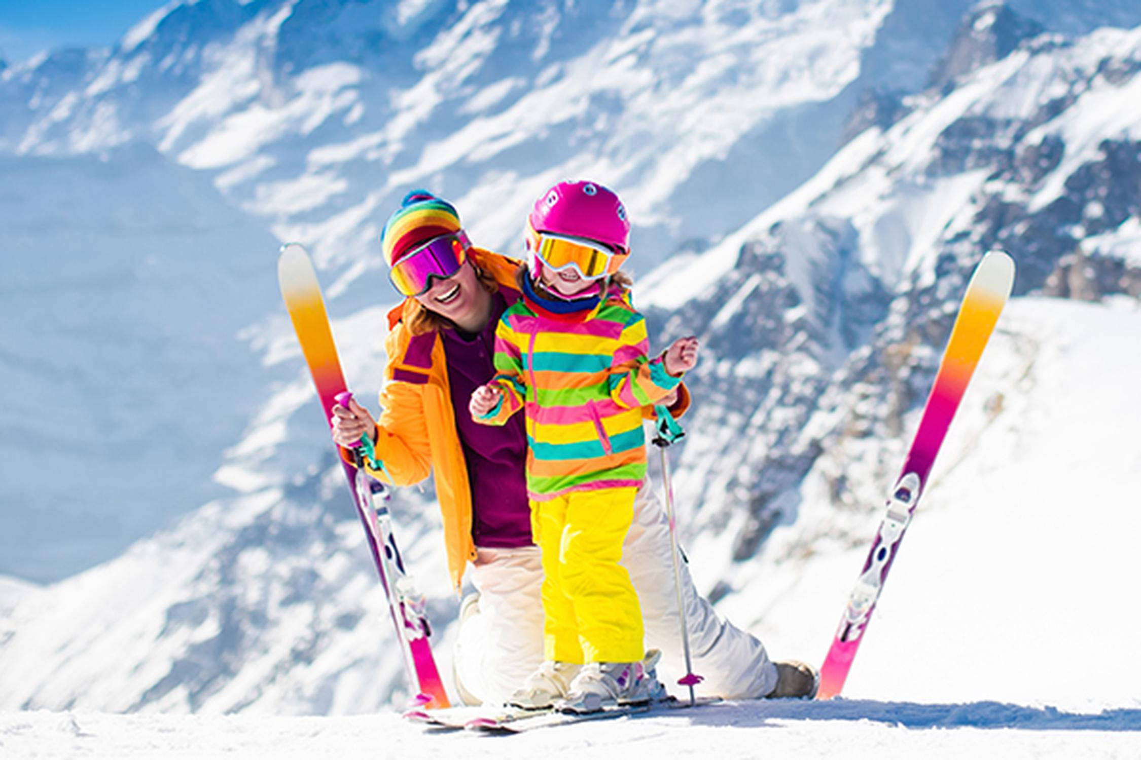 Eine Frau und ein Kleinkind mit Ski, Helm und Skibrille auf einer Skipiste