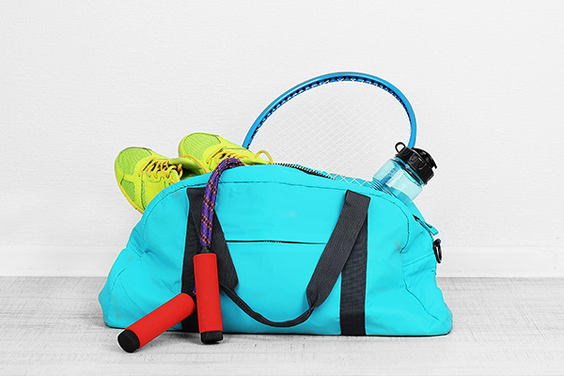 Türkise Sporttasche mit grünen Sportschuhen, einem blauen Tennisschläger, Wasserflasche und Springschnur mit rotem Griff