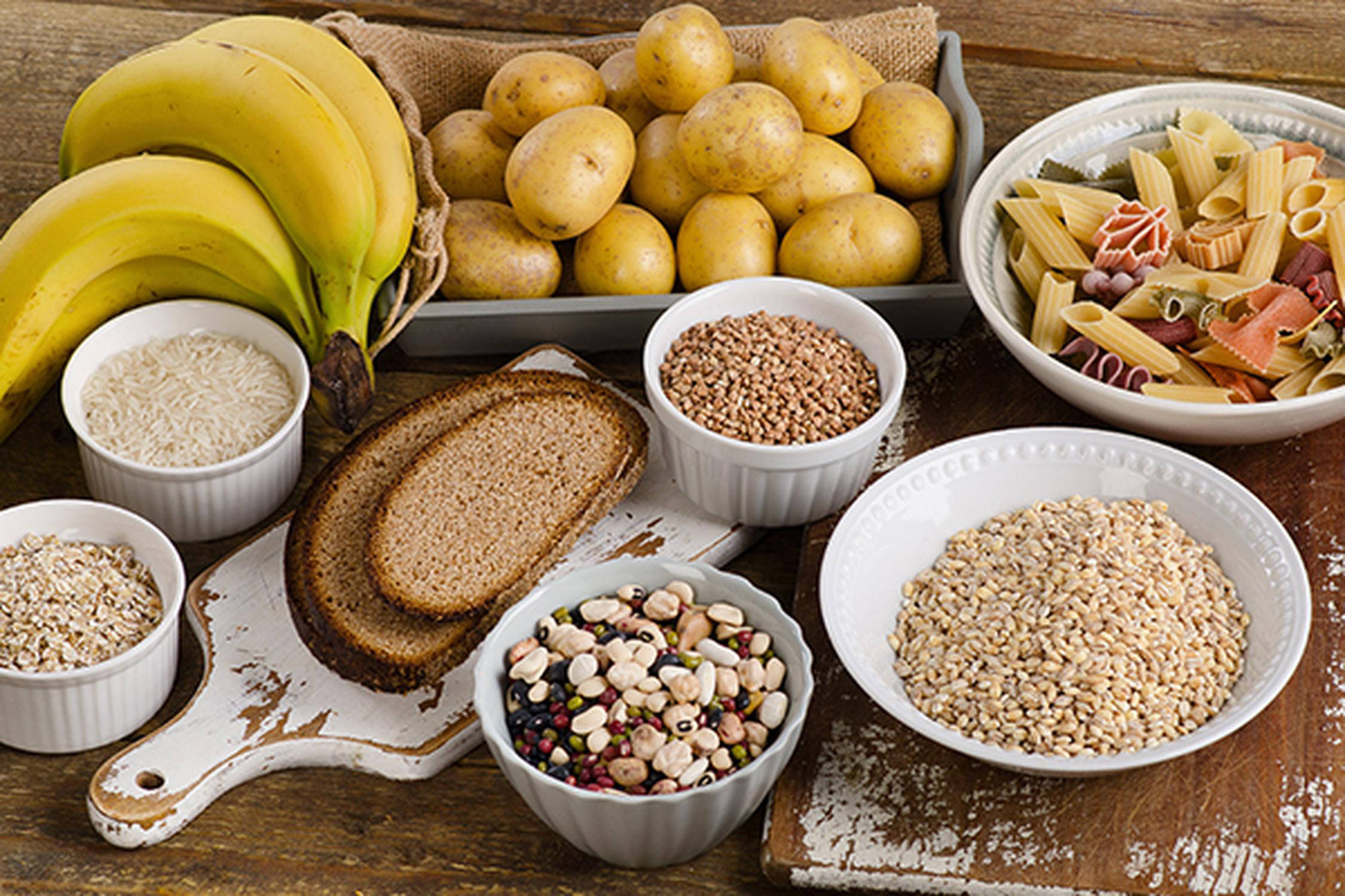 auf einem Tisch liegen Bananen, Brotscheiben, Kartoffel sowie Reis, Nüsse und Getreide in Schalen