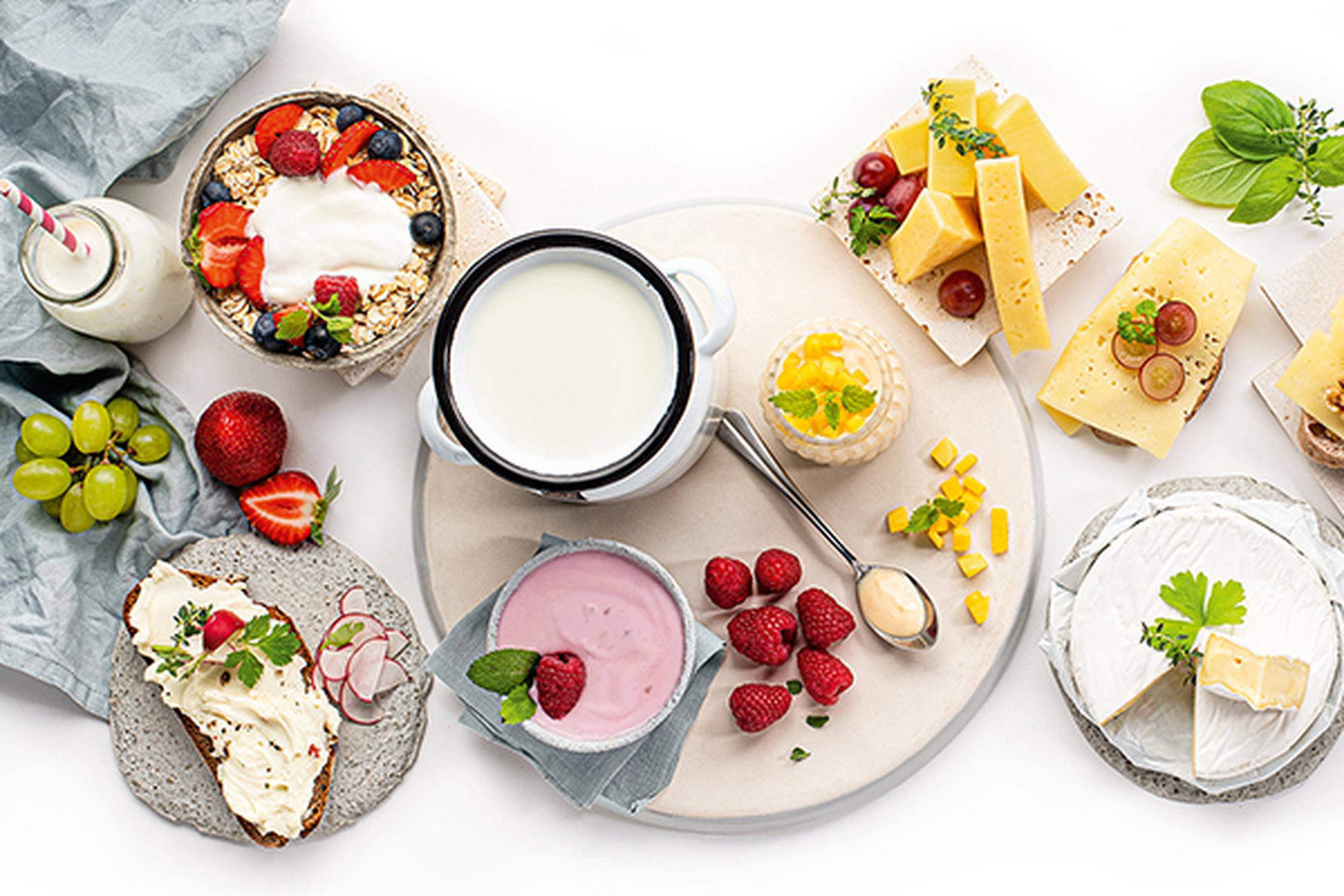 auf einem Tisch stehen Schüsseln und Teller mit Joghurt, Käse, Weintrauben und einem Glas mit Strohhalm