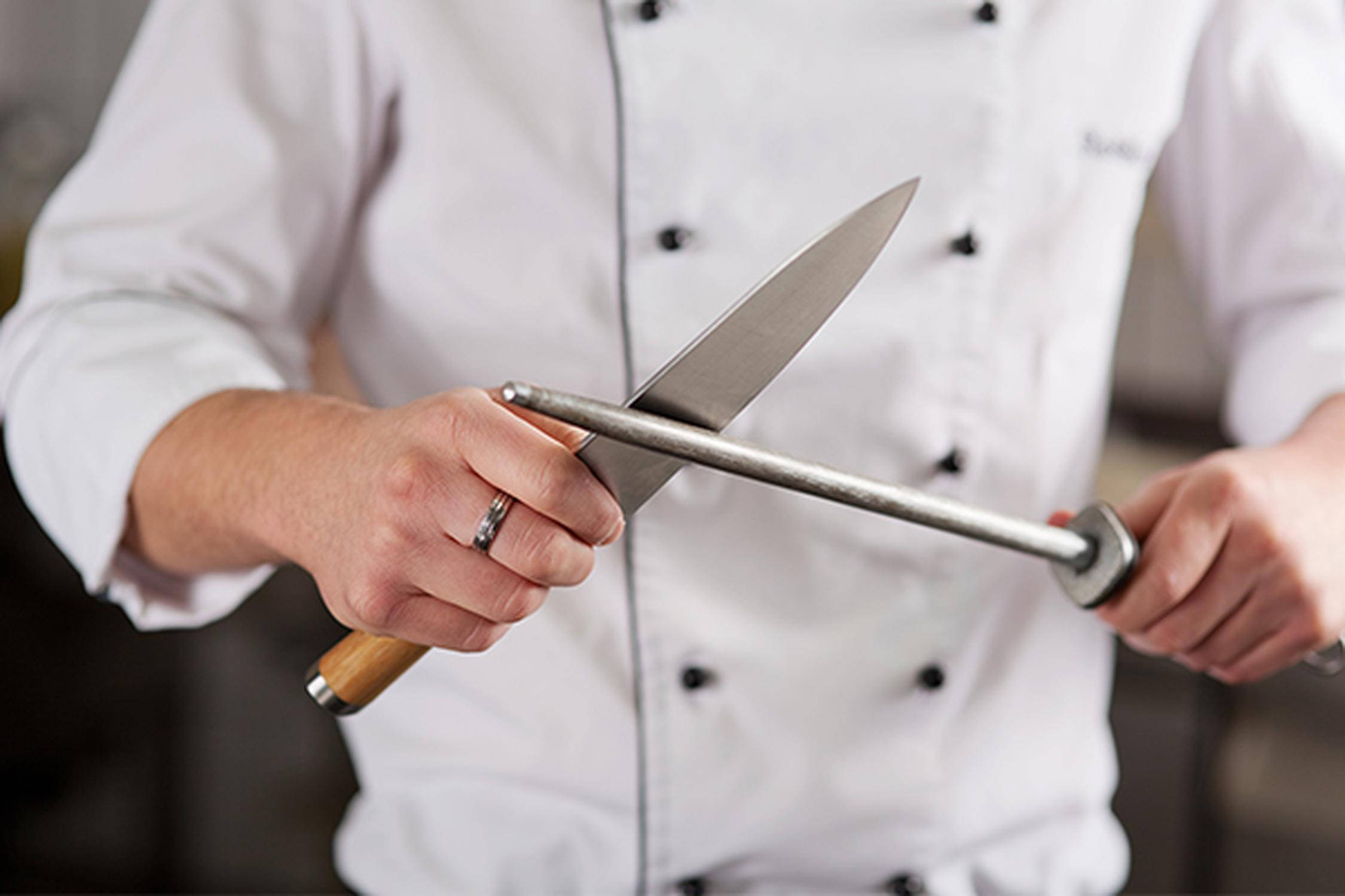Person hält in einer Hand einen Wetzstab und in der anderen ein Messer und schleift dieses