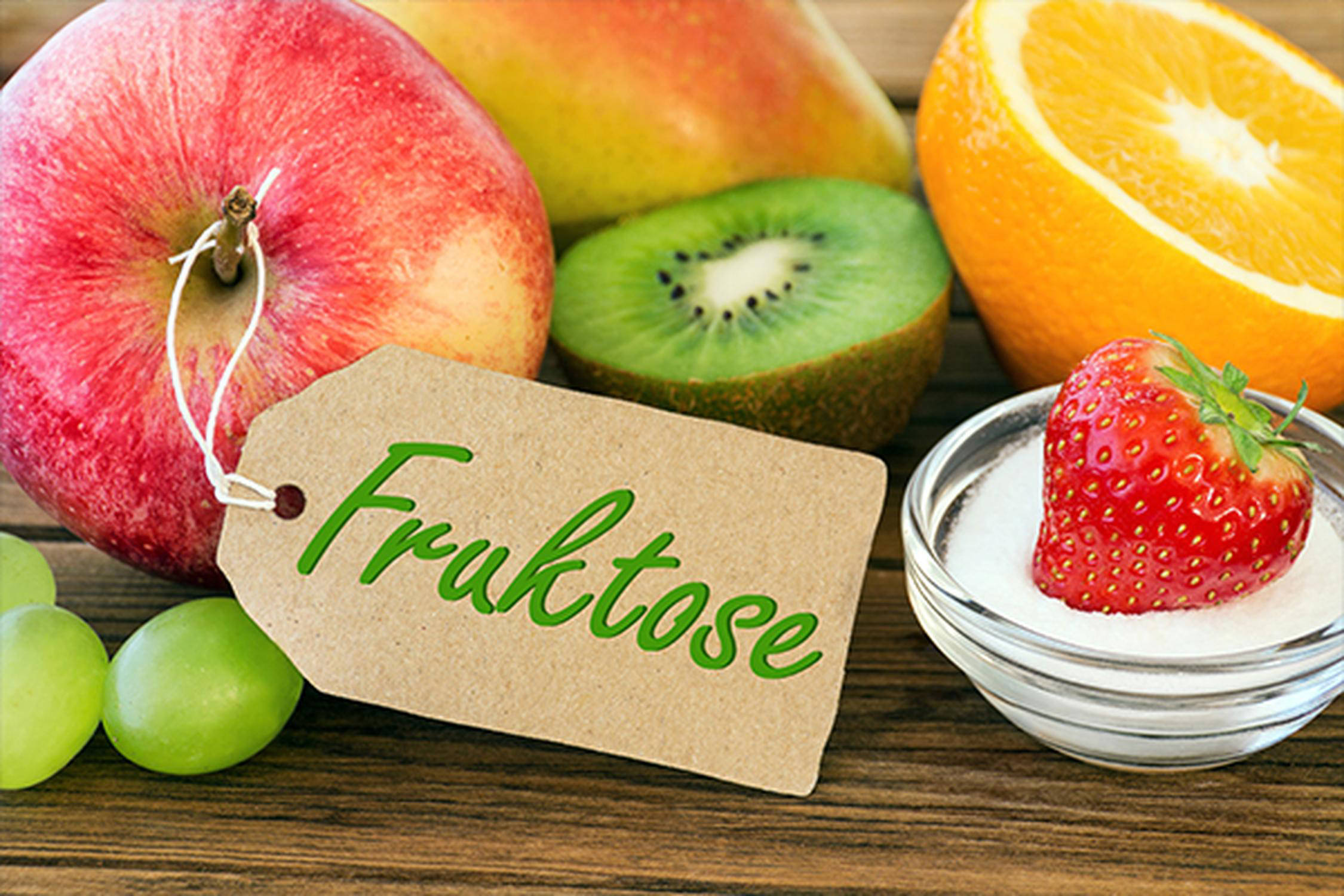 Apfel, Weintrauben, Kiwi, Orange, Erdbeere und ein Schild mit dem Wort "Fruktose"
