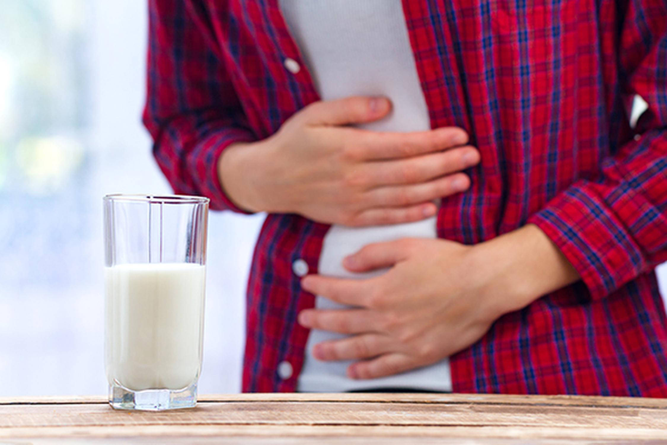Glas Milch steht auf einem Tisch, Person hält sich mit beiden Händen den Bauch