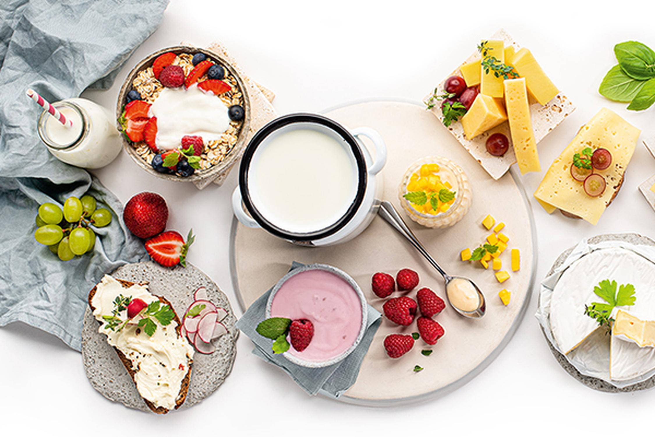 Drei kleine Formen mit Natur- und Beerenjoghurt gefüllt auf einer runden Platee, daneben Weintrauben, Beeren, ein Löffel
