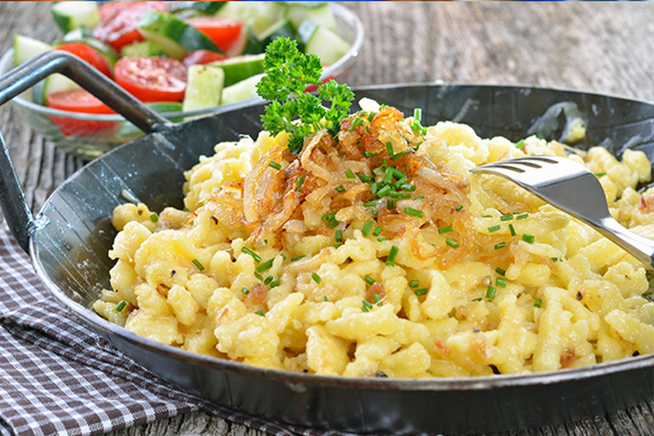 Pfanne mit Käsespätzle und daneben eine Schüssel mit gemischtem Salat