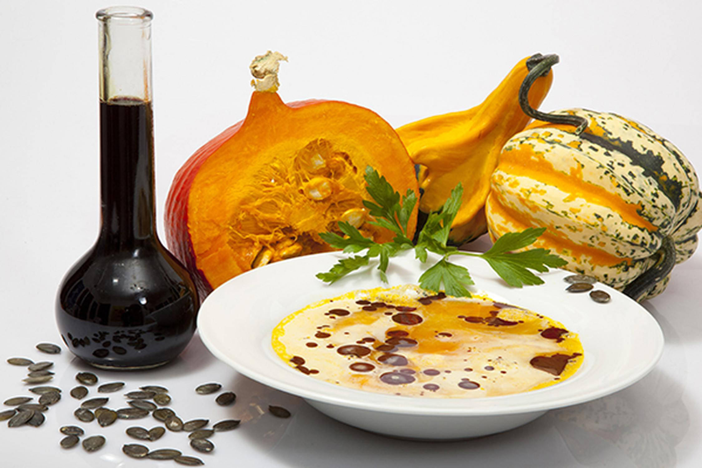 Suppenschüssel mit Kürbissuppe, dahinter eine Flasche Kernöl und drei Kürbisse