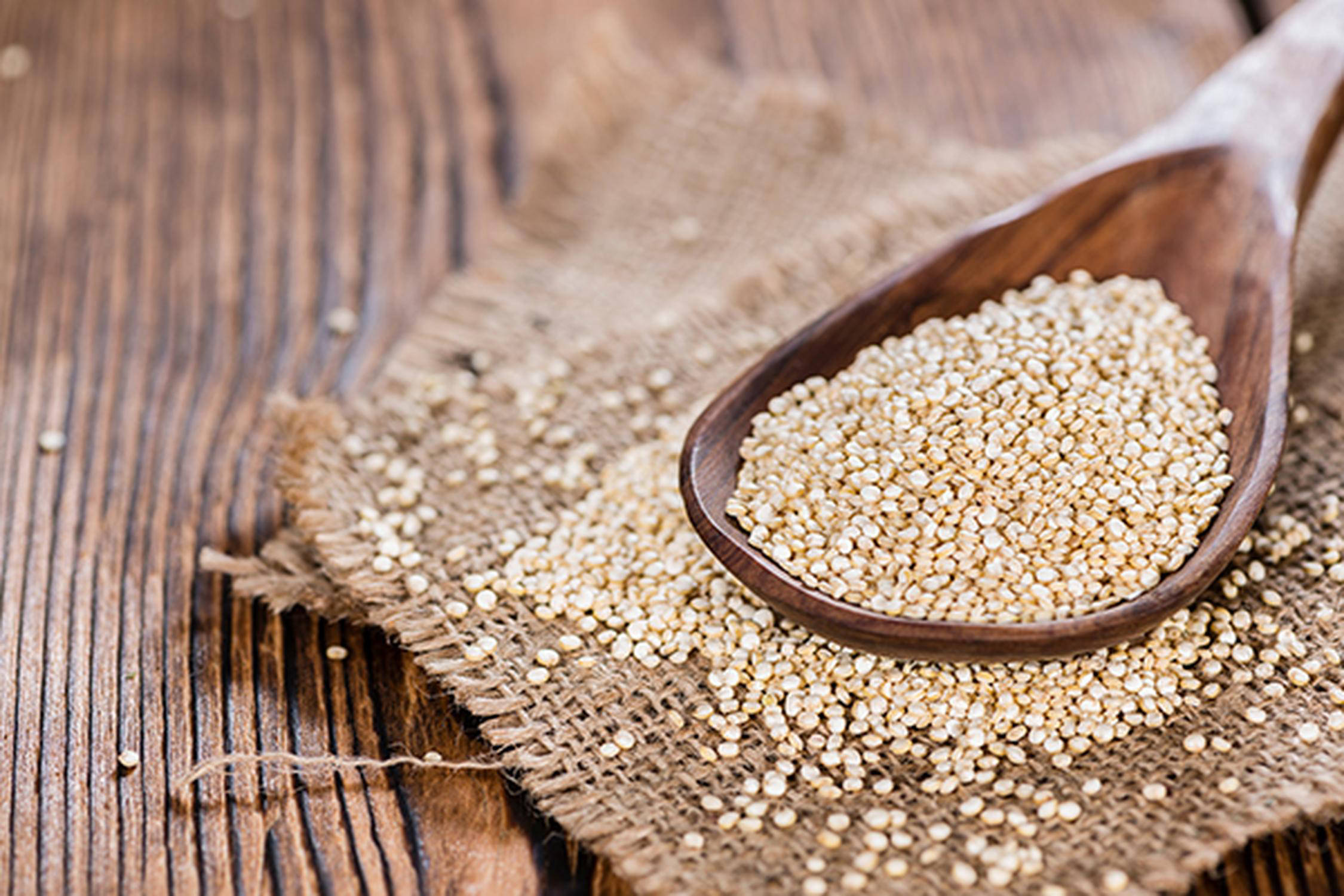 Quinoa auf einem Holzlöffel, der auf einem Jutestück auf einem Holztisch liegt