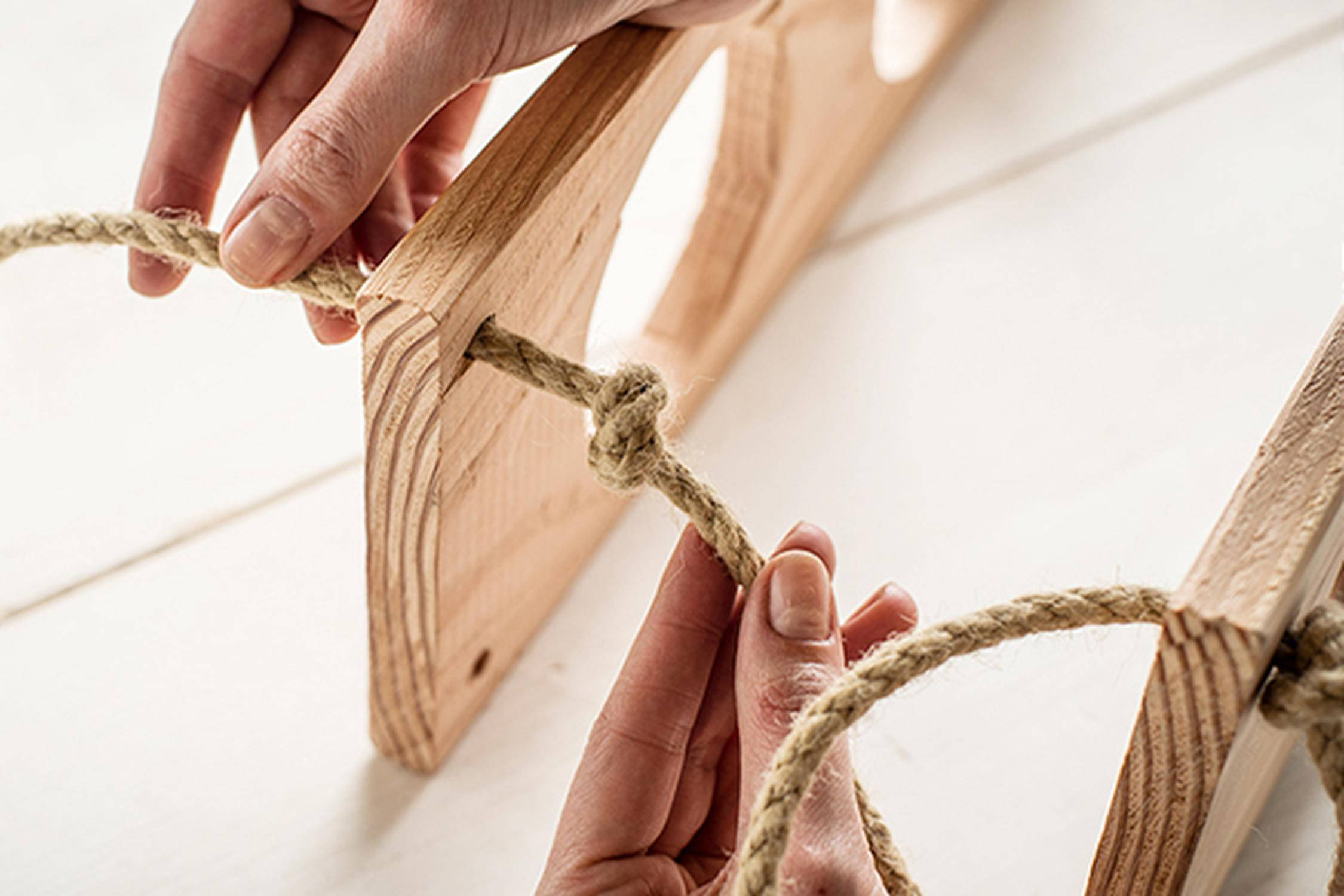 Zwei Hände befestigen ein Seil an zwei Holzplatten
