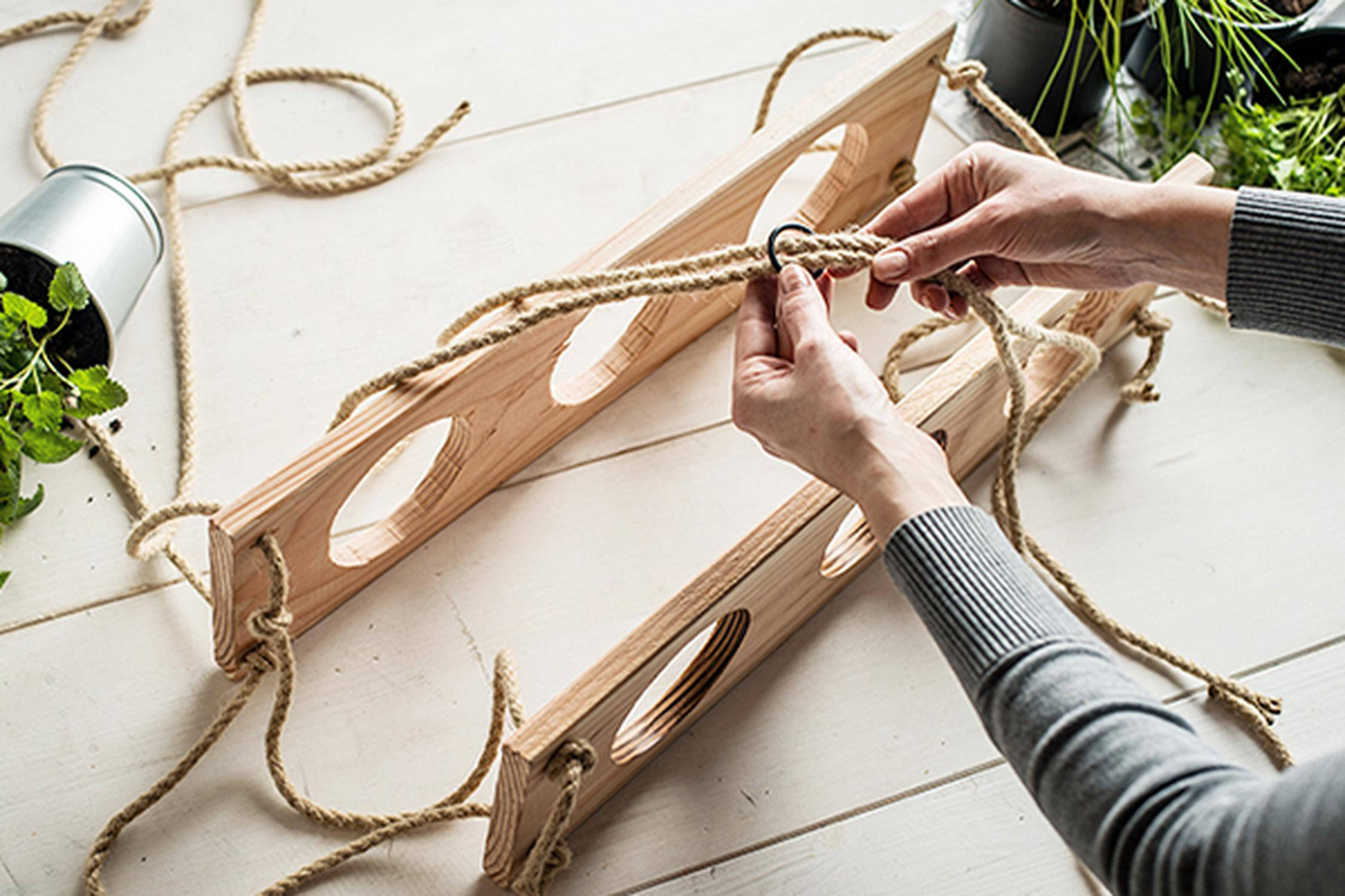 Zwei Hände hängen zwei Holzplatten mit Schnüren zusammen und befestigen einen Ring