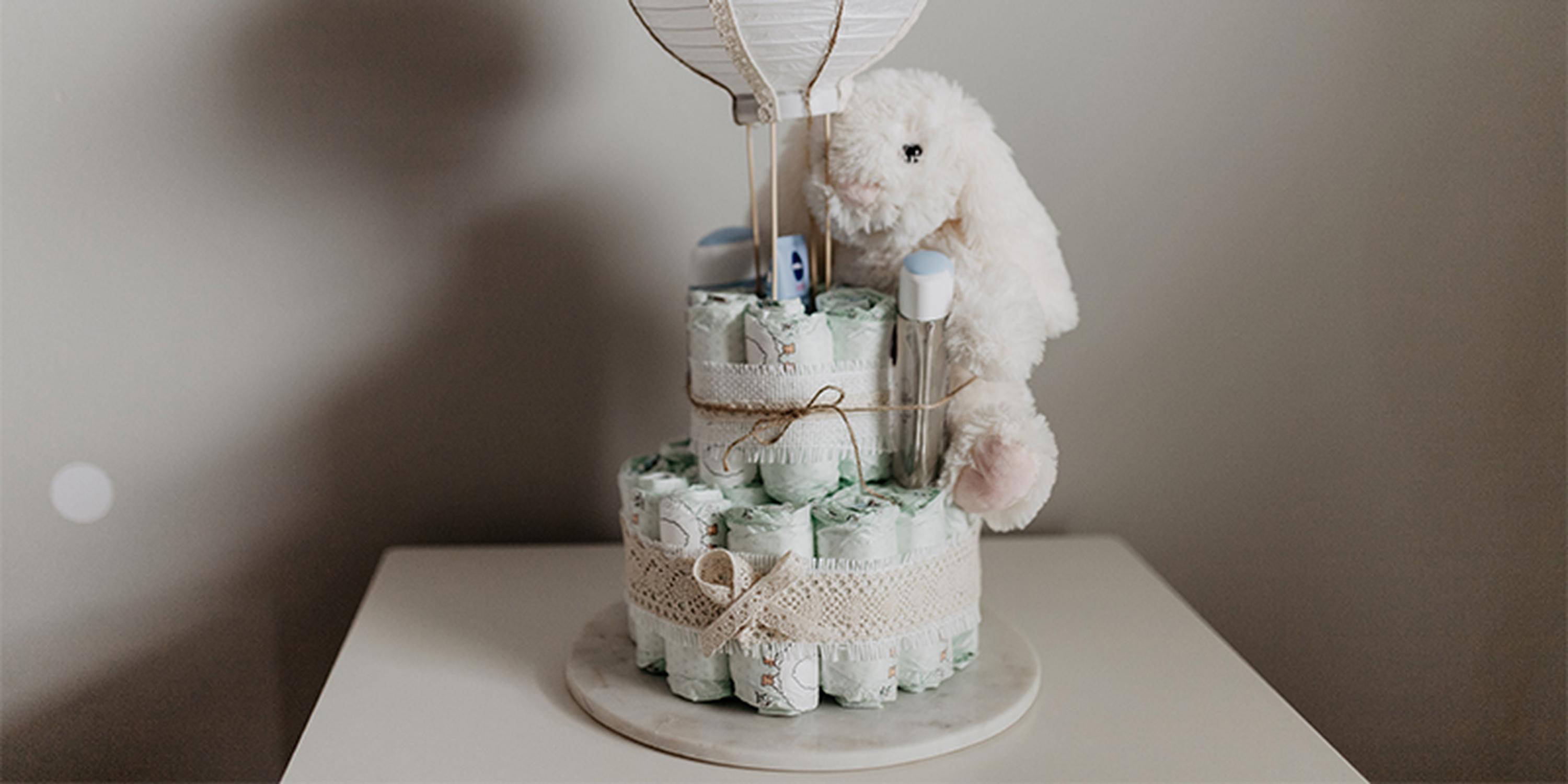 Windeltorte mit weißem Stoffhasen und Papierballon auf einem weißen Tisch