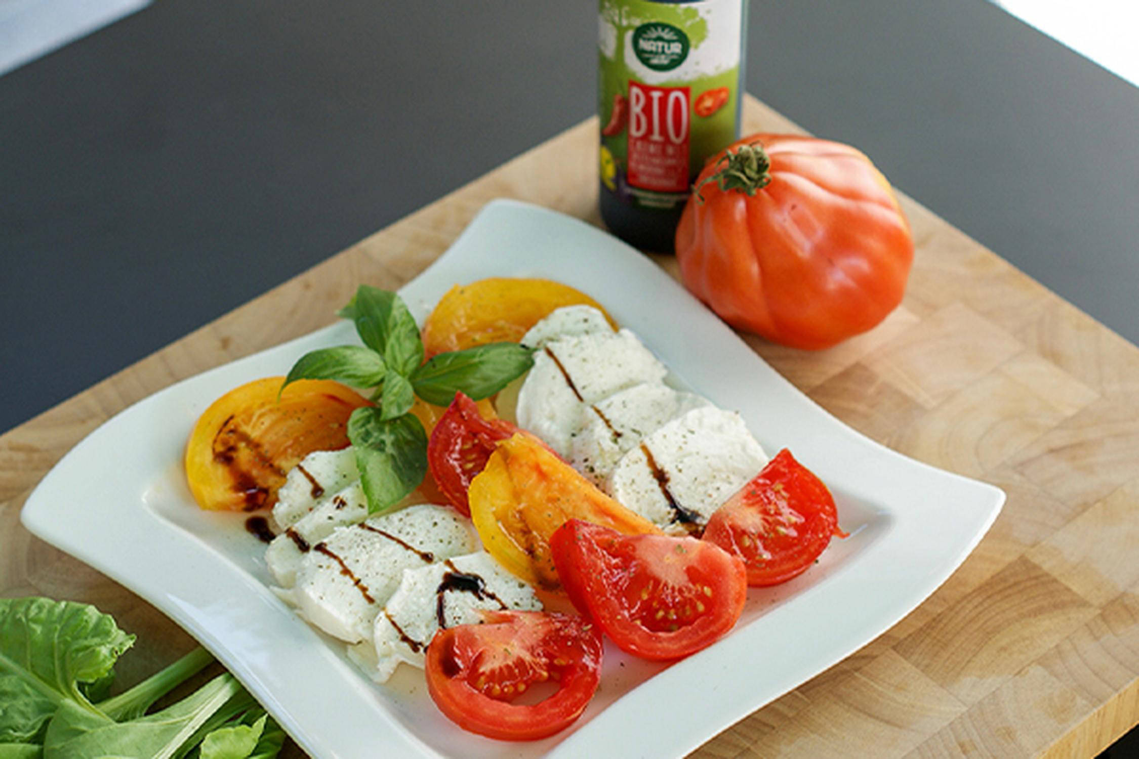 Auf einem weißen Teller liegen Mozzarella und Tomaten in Scheiben geschnitten mit Essig und Basilikum garniert