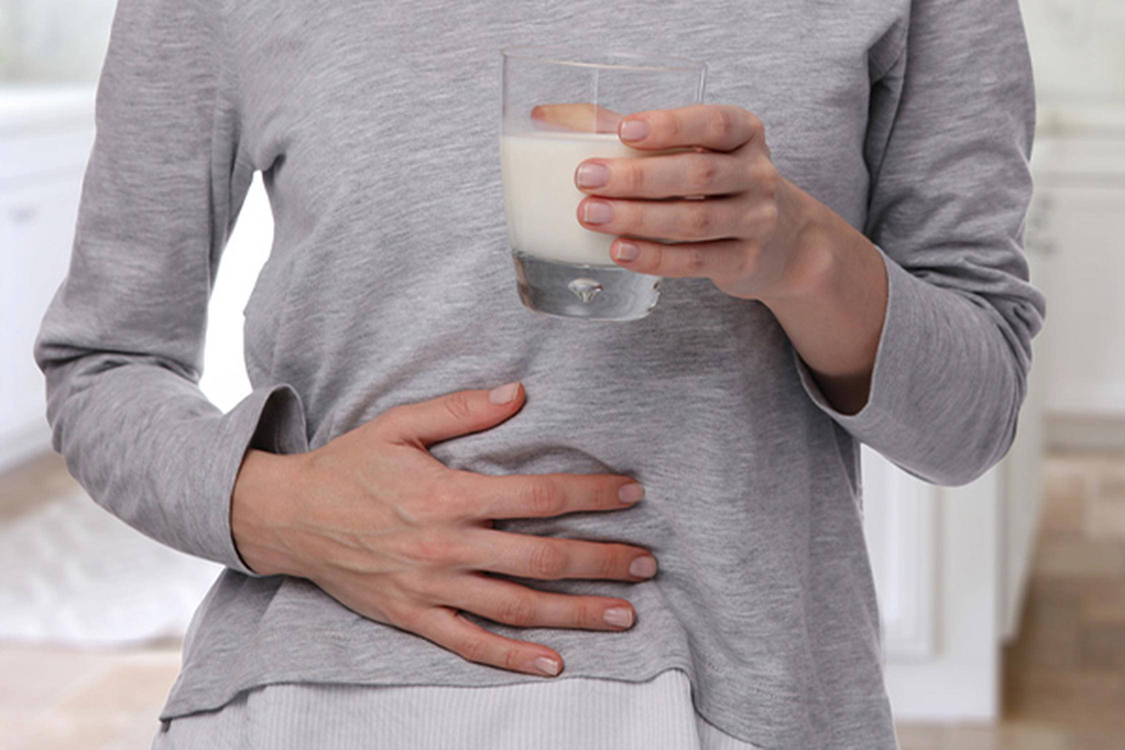 Person hält sich mit einer Hand auf den Bauch und in der anderen Hand ist ein Glas mit Milch