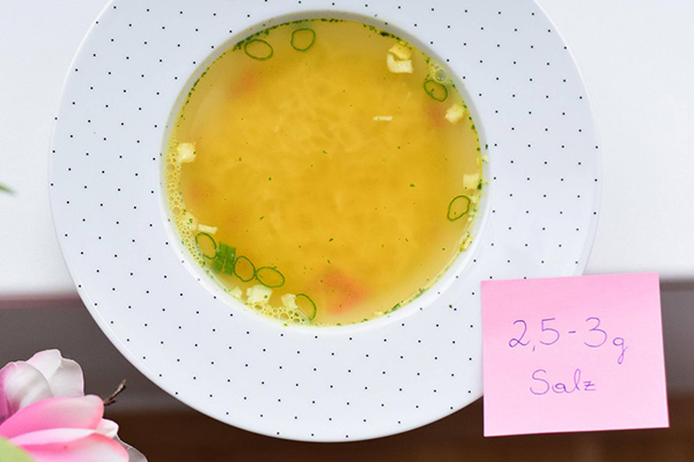 Klare Suppe in einer Schüssel und einem rosa Post-It "2,5-3 g Salz"