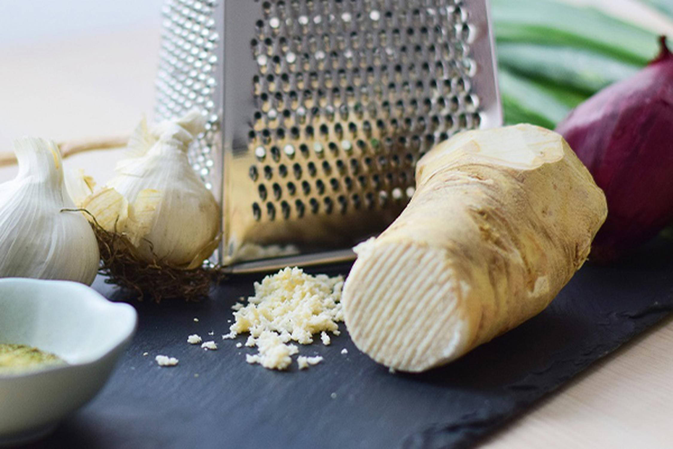 Schiefersteinplatte mit zwei Knoblauchknollen, Reibe und Krenwurzel und geriebenem Kren