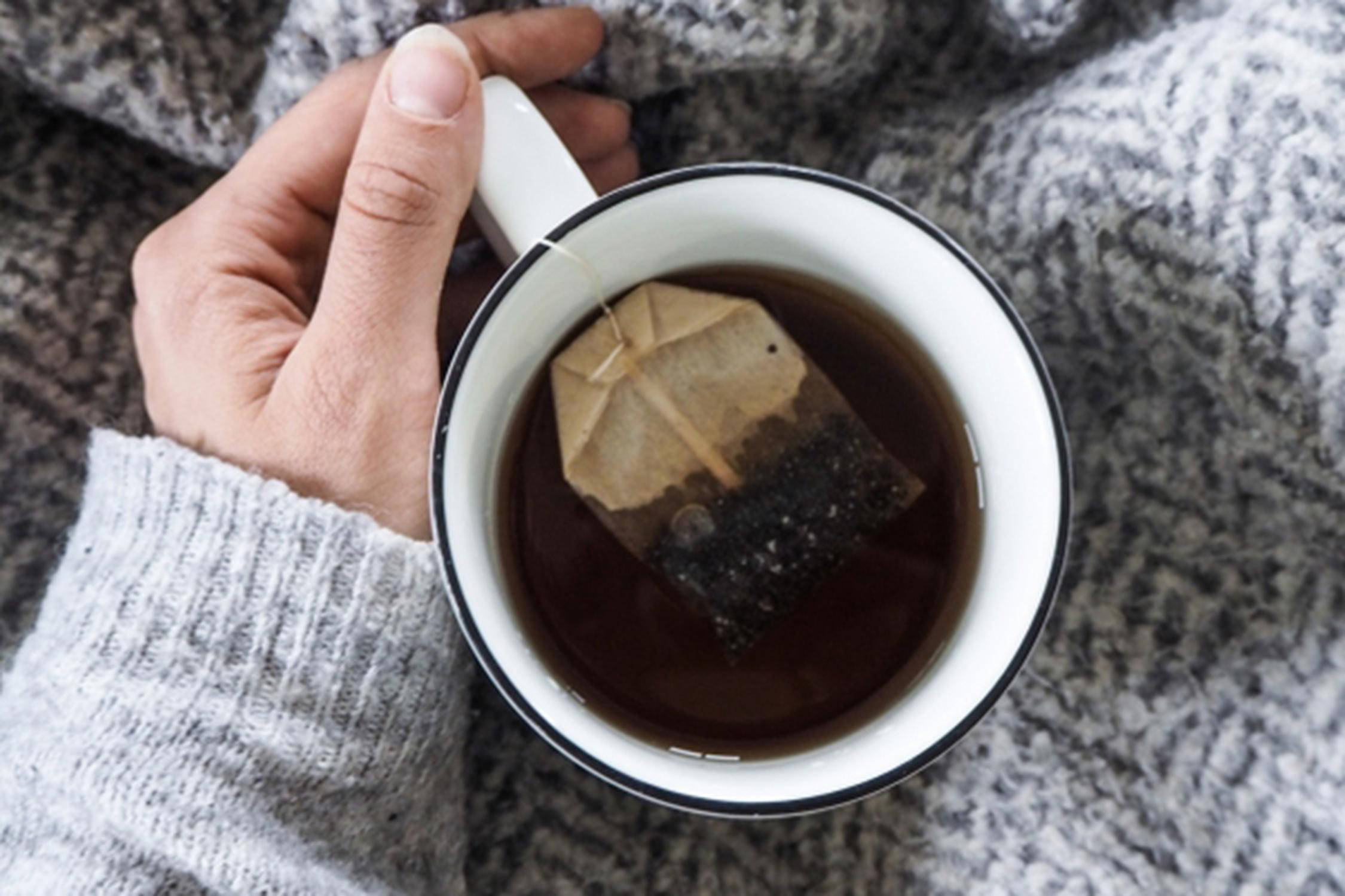 Hand hält eine Tasse mit Tee und Teebeutel.