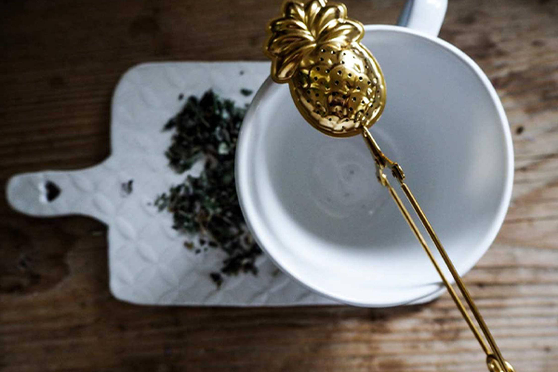 goldenes Teeei in Form einer Ananas über eine weiße Tasse gelegt.