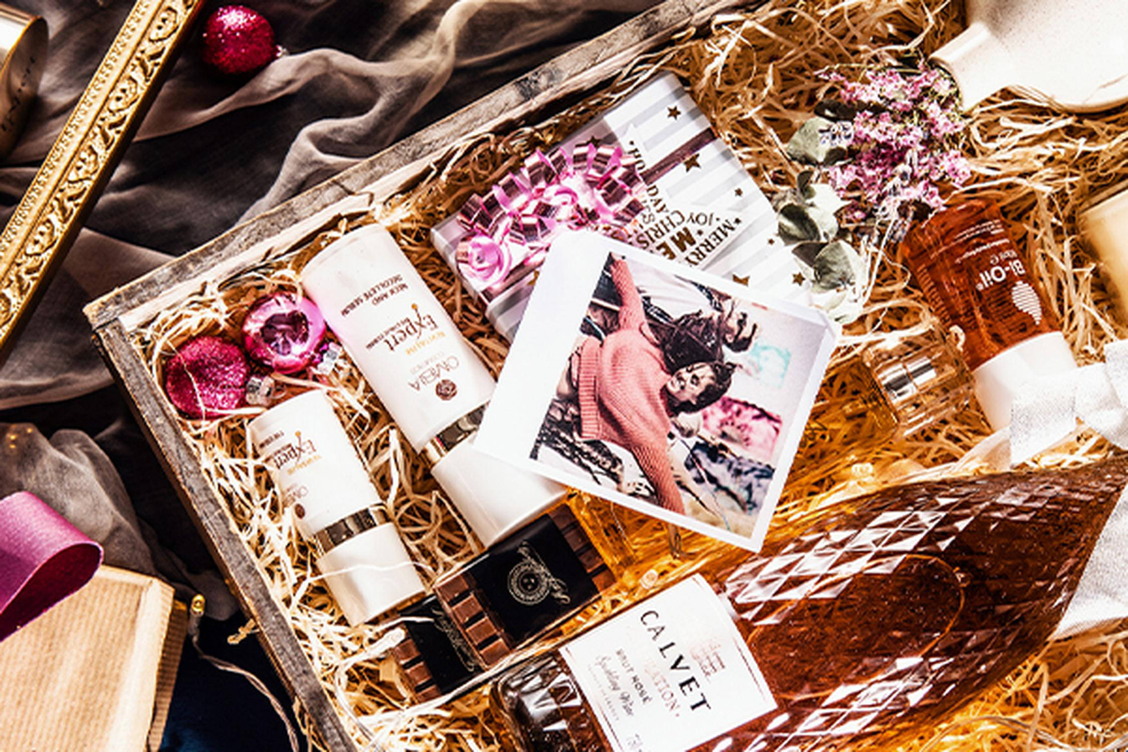 Geschenkbox mit verschiedenen Flaschen, pinken kleinen Christbaumkugeln und einem Polaroidfoto