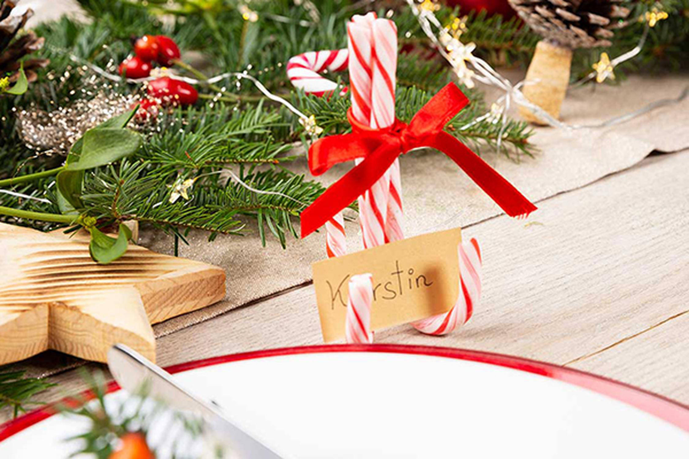 Zuckerstangen als Halterung für ein Namenskärtchen neben einem weißen Teller mit rotem Rand