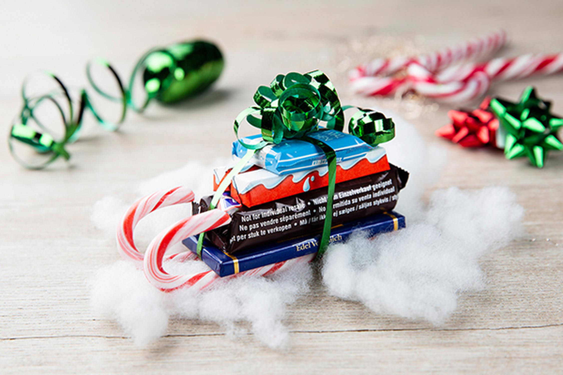 kleiner selbst gebastelter Schlitten mit Süßigkeiten dekoriert mit Watte, Zuckerstangen und Geschenkband