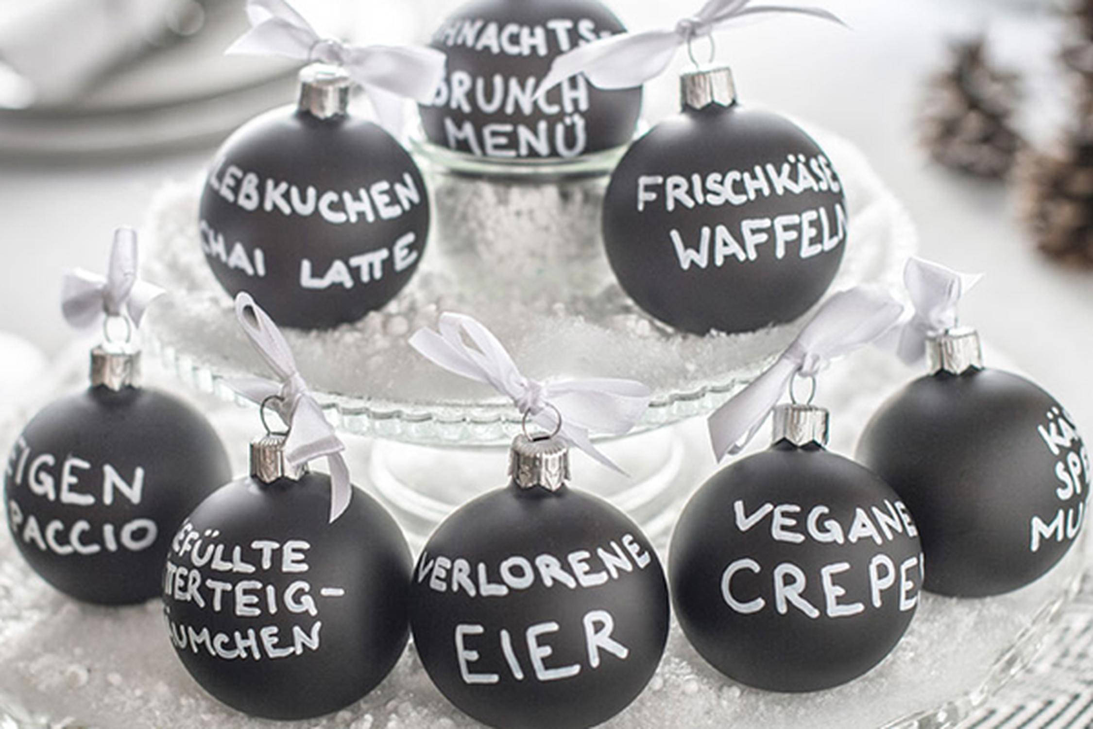 schwarze Christbaumkugeln mit je einem Gang eines Menüs in weißer Schrift