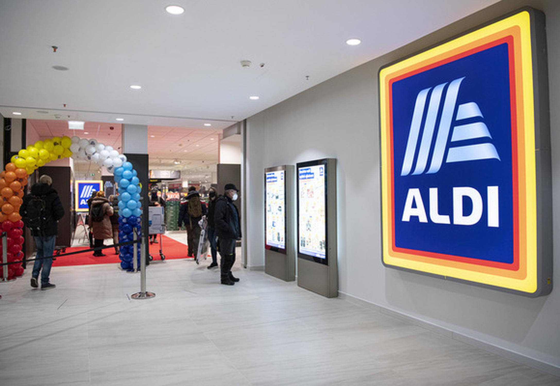 Az ALDI két munkatársa újhagymás ládákat tesz a zöldséges polcokra.