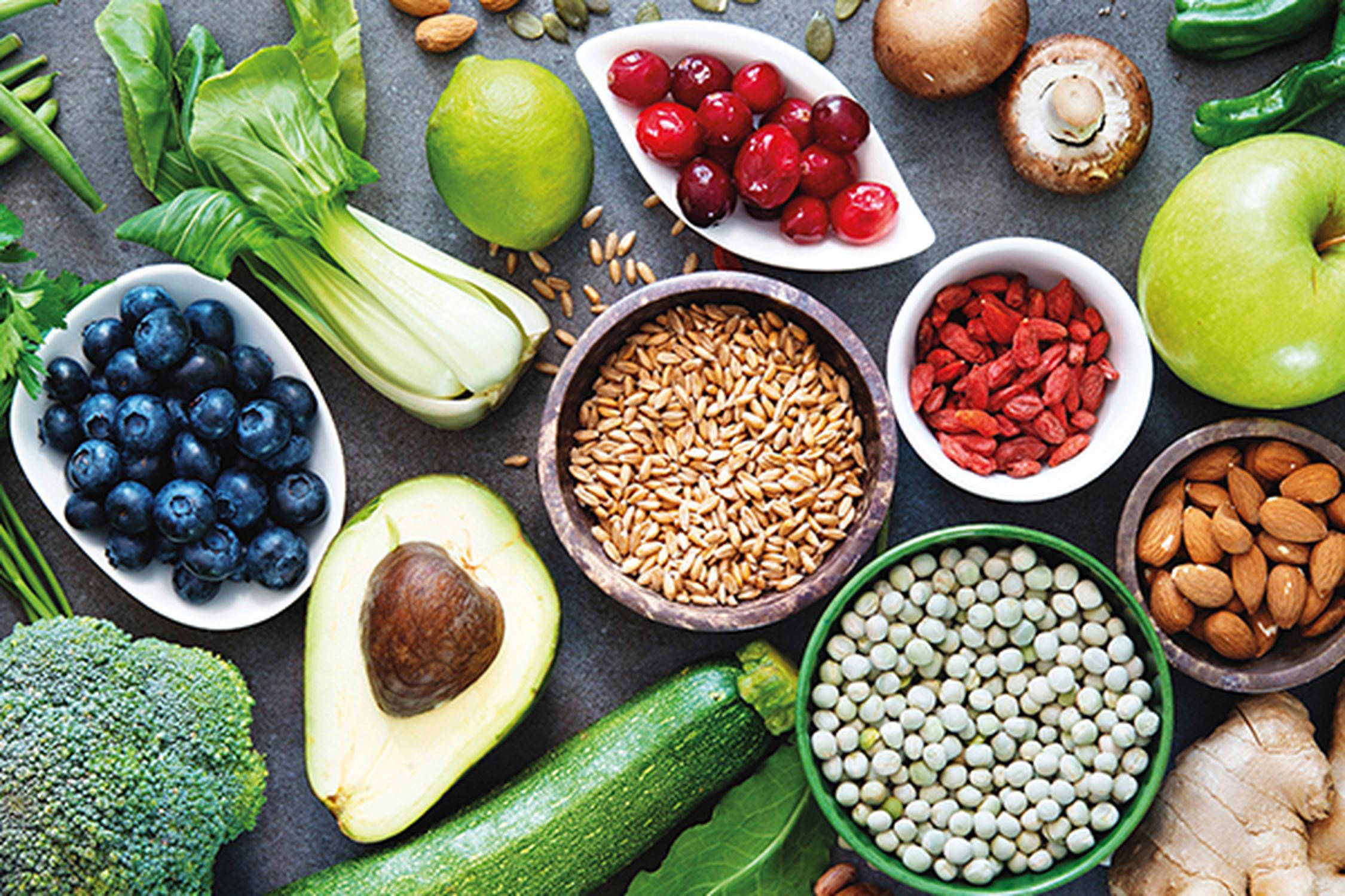 verschiedenes Obst, Gemüse und Nüssen liegen auf einem grauen Untergrund