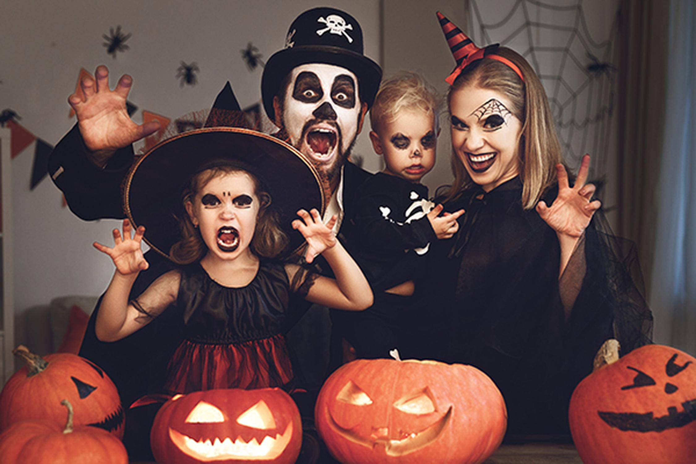 Eine Frau, ein Mann und zwei Kinder sind für Halloween verkleidet; vier geschnitzte Kürbisse stehen im Vordergrund
