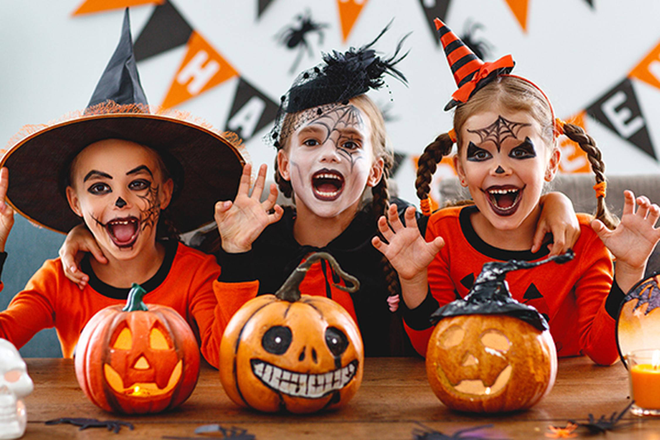 drei verkleidete Kinder für Halloween, im Vordergrund stehen drei kleine geschnitzte Kürbisse