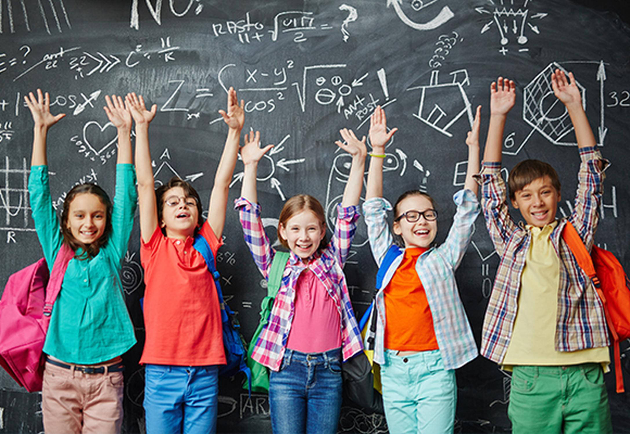 Schulkinder stehen vor einer Tafel und halten die Hände in die Höhe