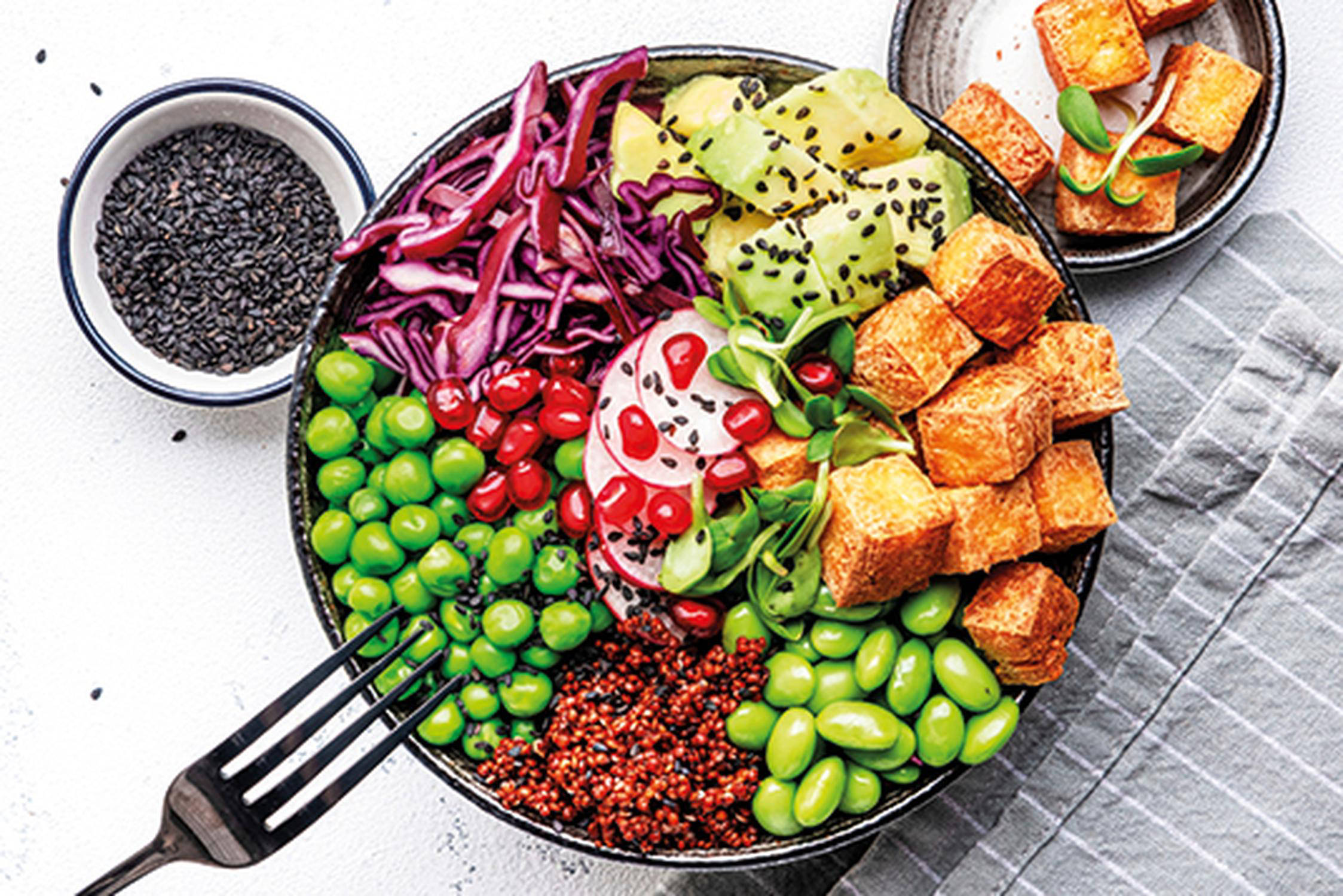 Bowl gefüllt mit Tofu, Avocado, Quinoa, Edamame und Salat, Gabel lehnt an der Schüssel