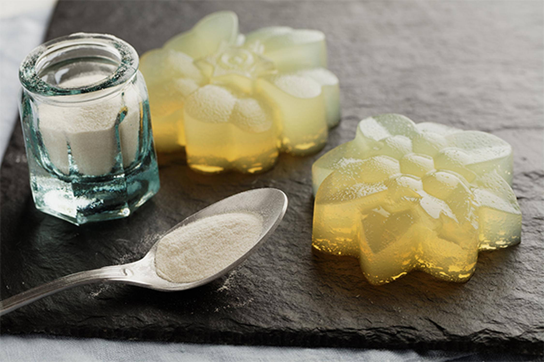 auf einer Schieferblatte liegt ein Löffel, ein kleines Glas und zwei Stück Gelatine-Blumen