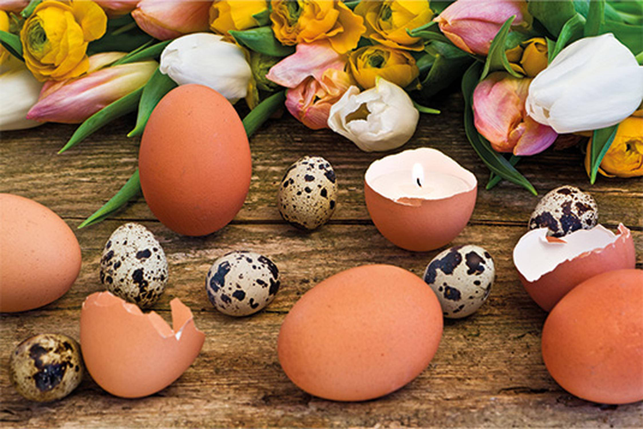 Eier-Kerzen und ganze Eier, im Hintergrund liegen bunte Schnittblumen