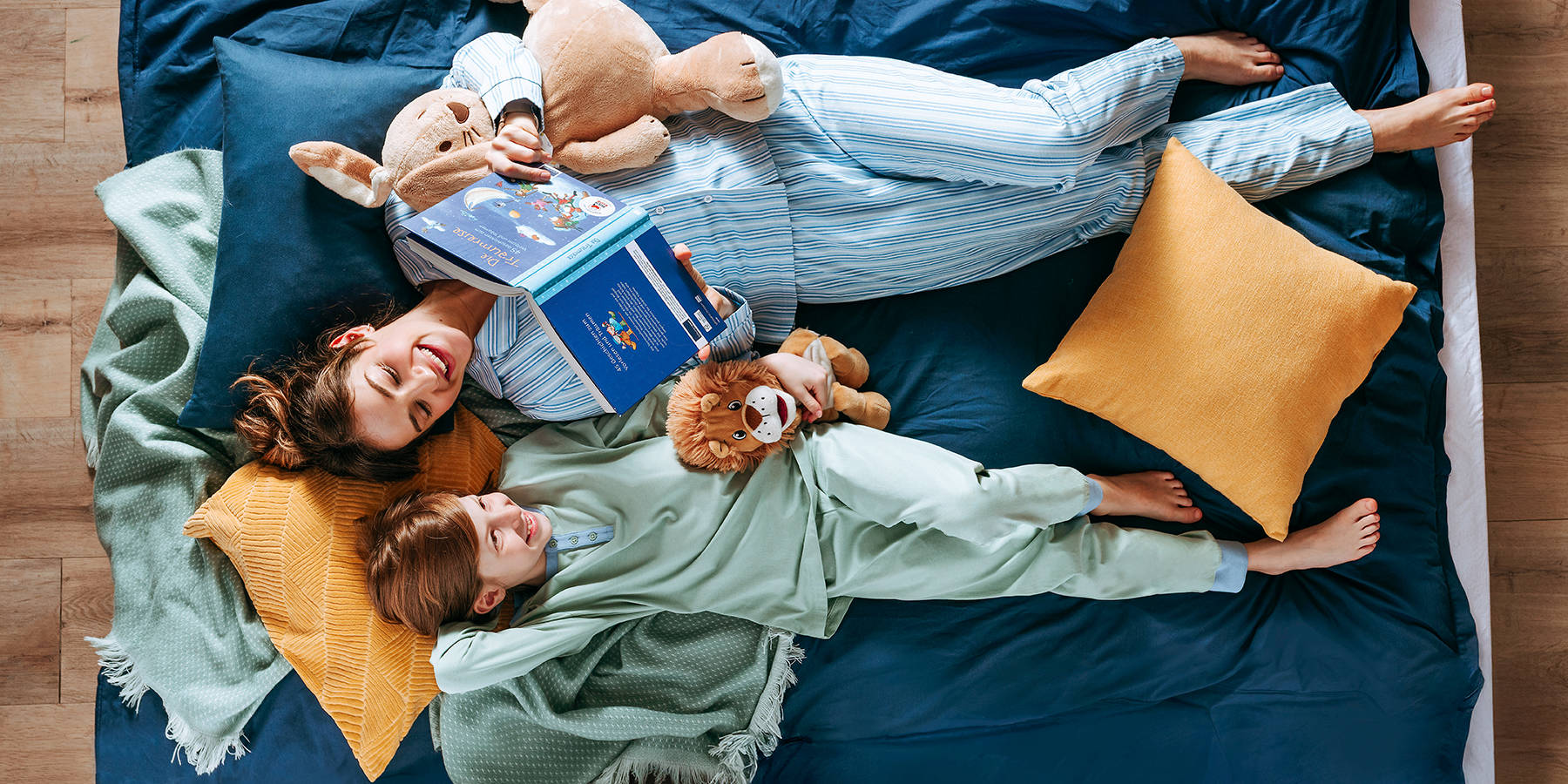 Mamica in hči ležita v postelji in gledata knjigo, oblečeni sta v pižami