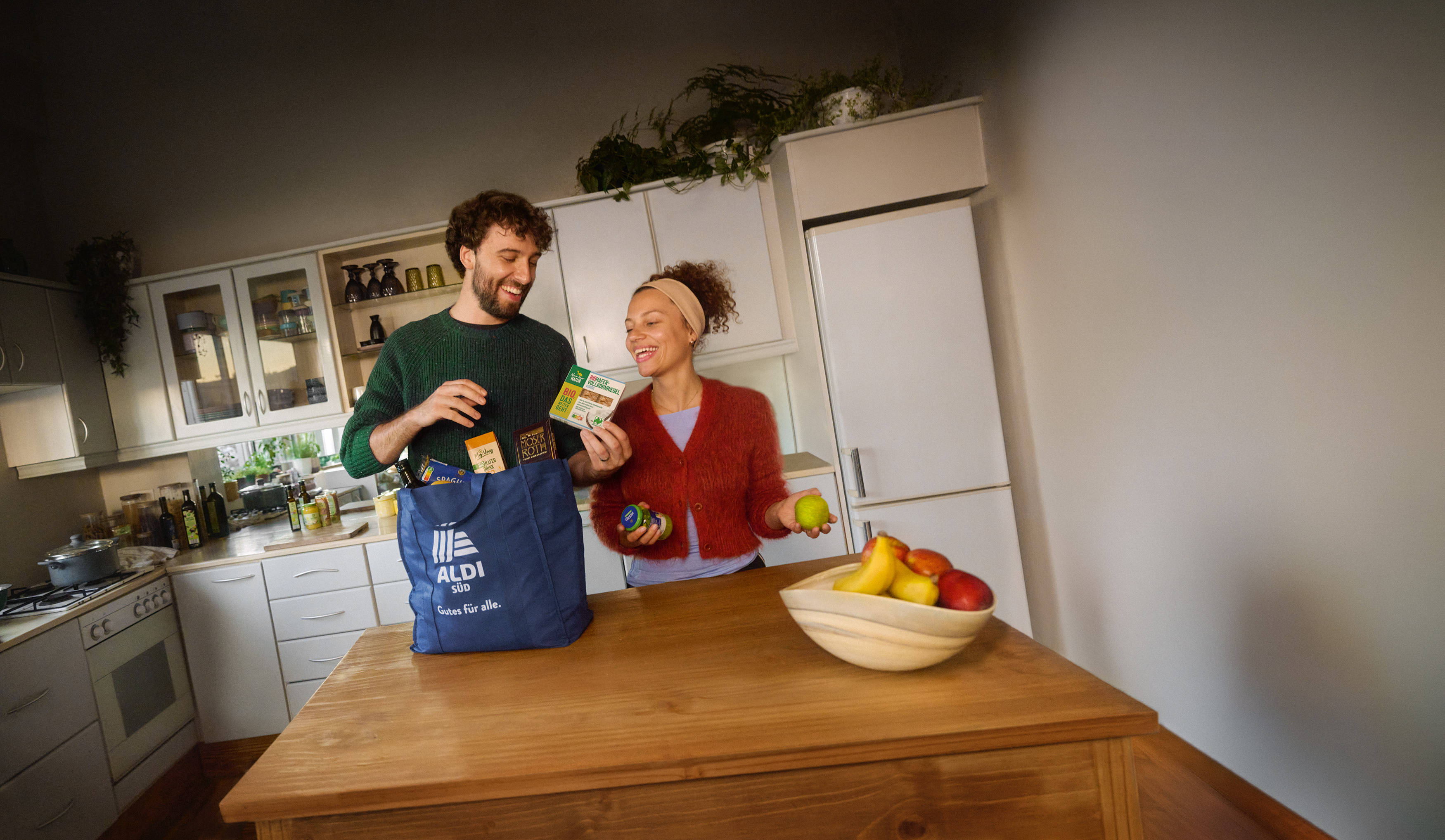 Mann und Frau stehen mit einer vollen ALDI Einkaufstüte am Küchentisch