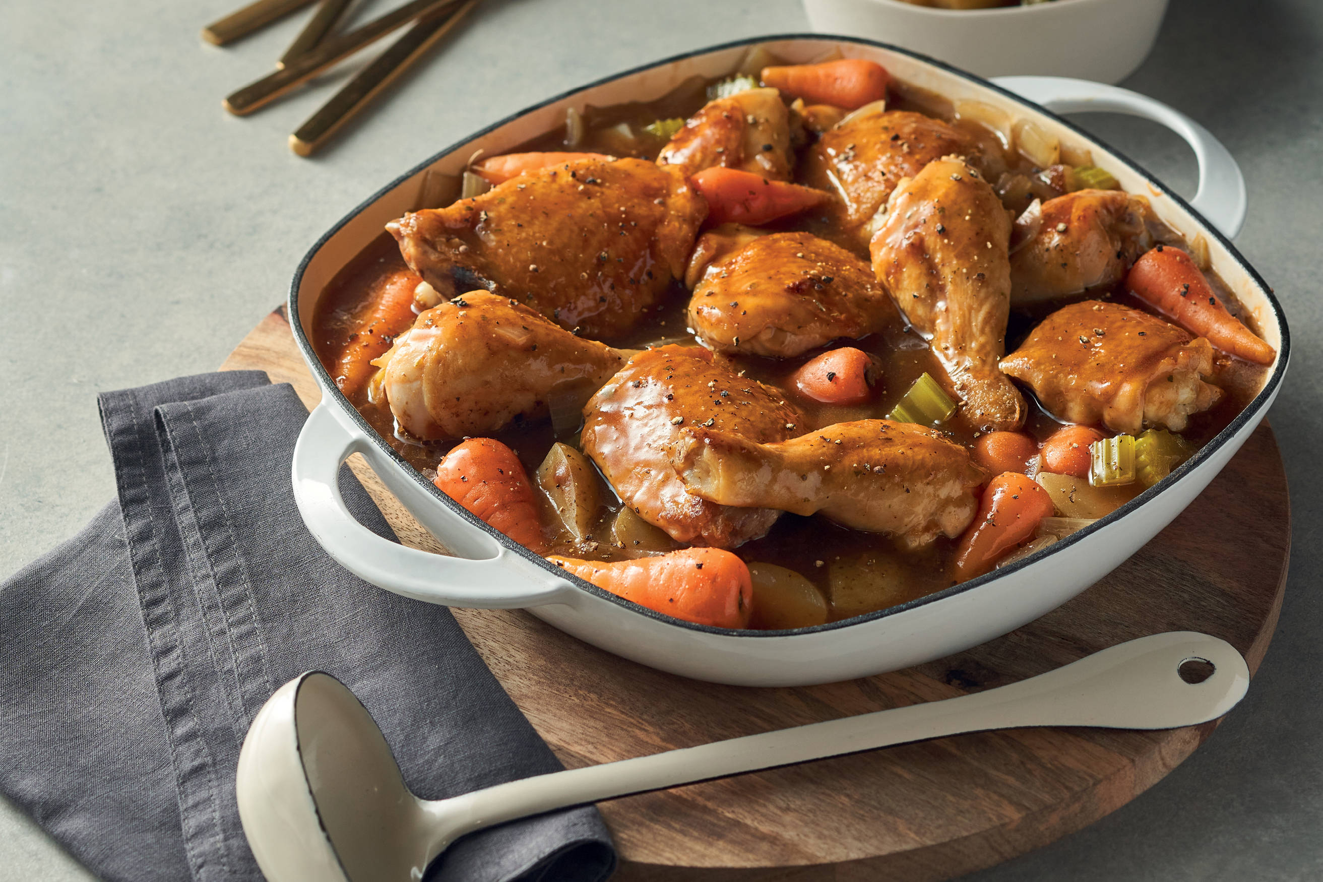 A white bowl containing a classic chicken casserole recipe on a table with a towel, spoon and wooden board.
