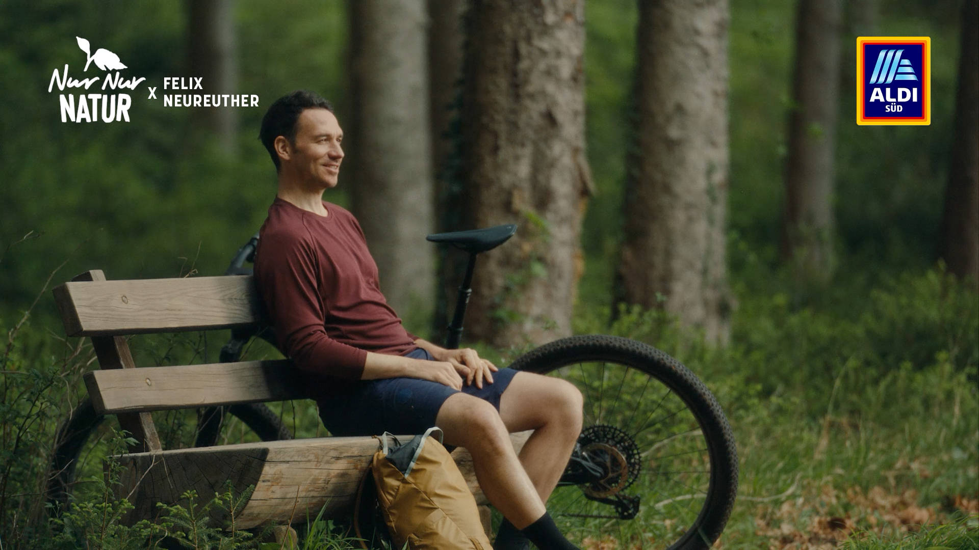 Felix Neureuther sitzt auf einer Bank im Wald, neben ihm steht sein Fahrrad.