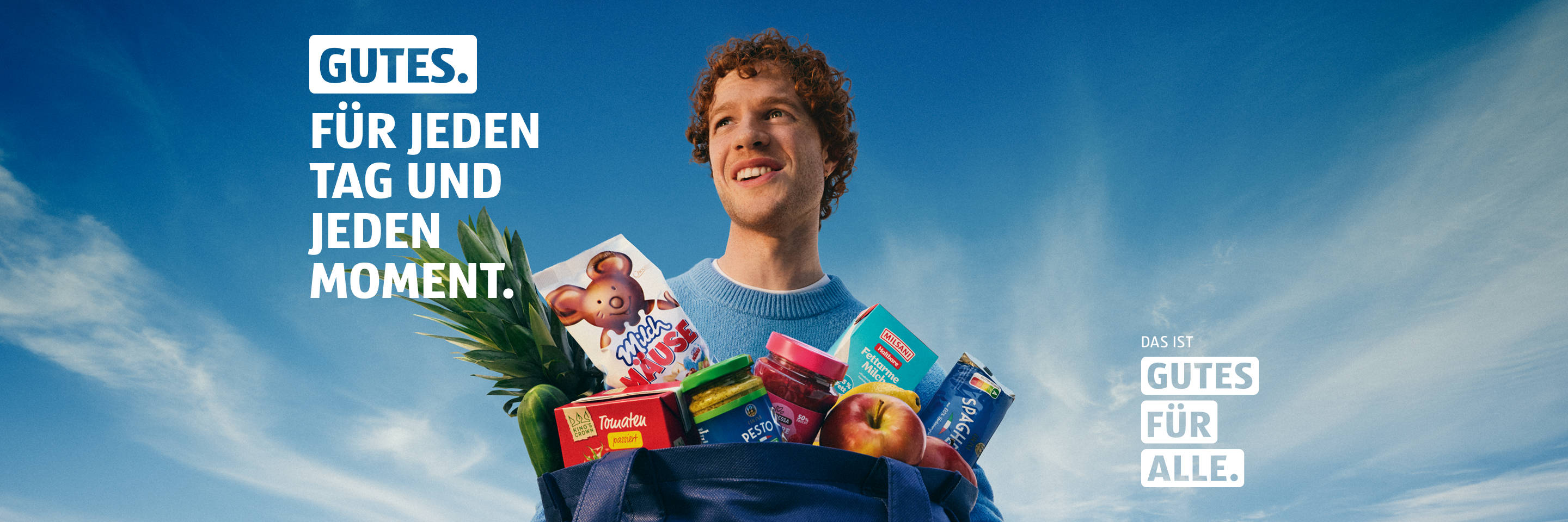 Person mit Einkaufstasche voller ALDI Produkte vor blauem Himmel.