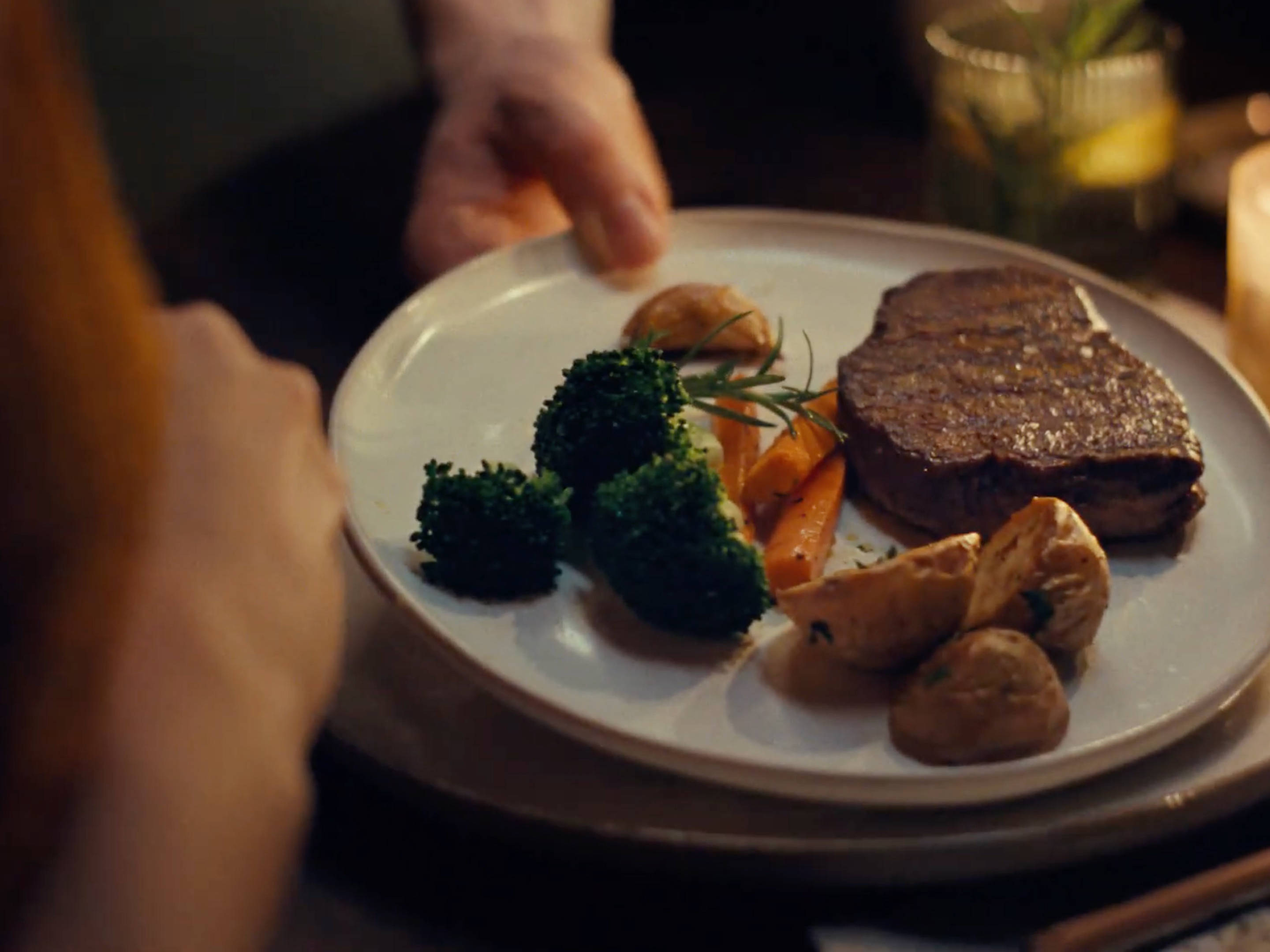 Ein Teller mit Steak, Kartoffeln und Brokkoli wird auf einem Esstisch serviert.