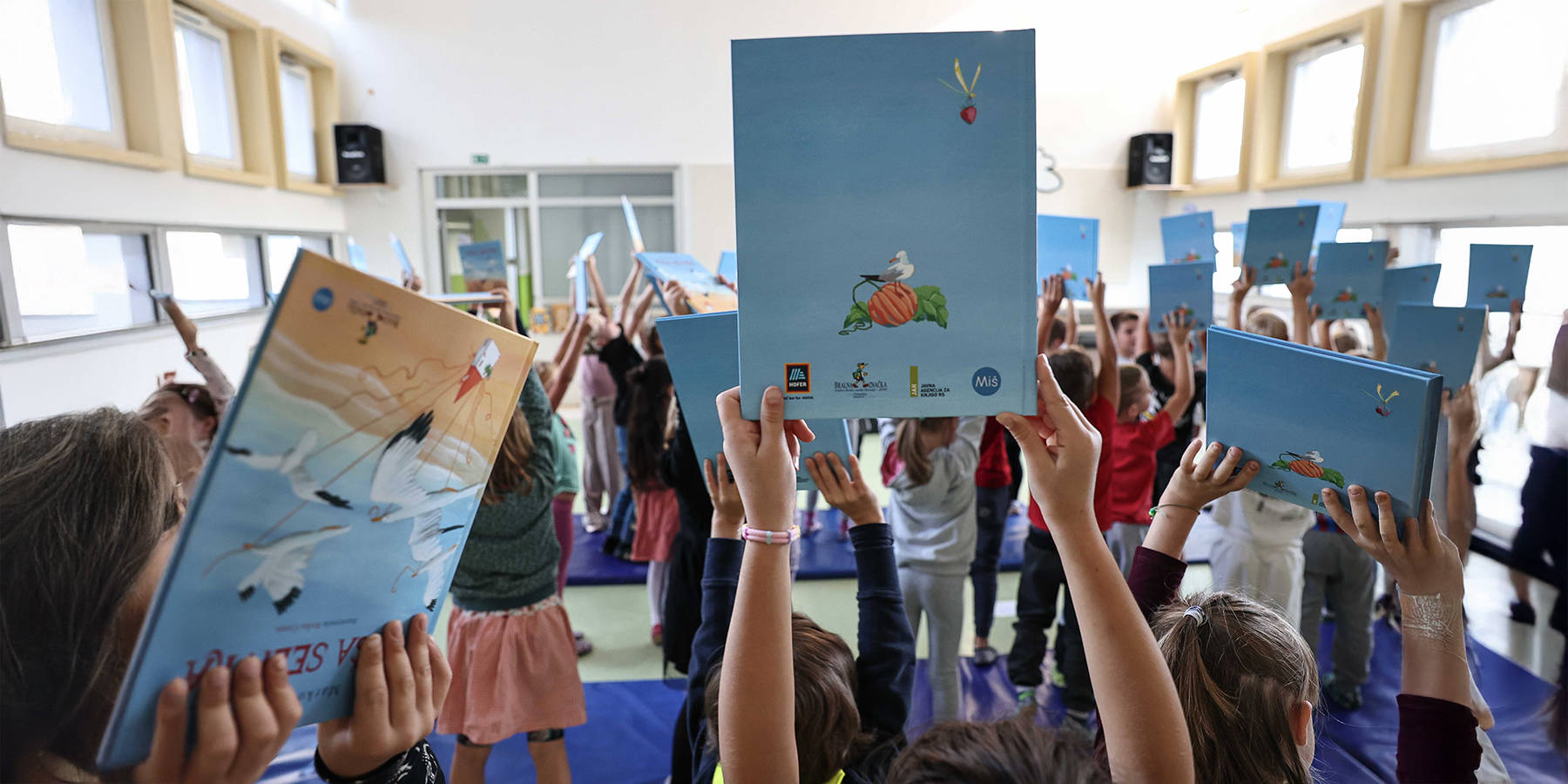 Otroške roke držijo mapice v ozadju, napis: Pomagamo mnogim otrokom