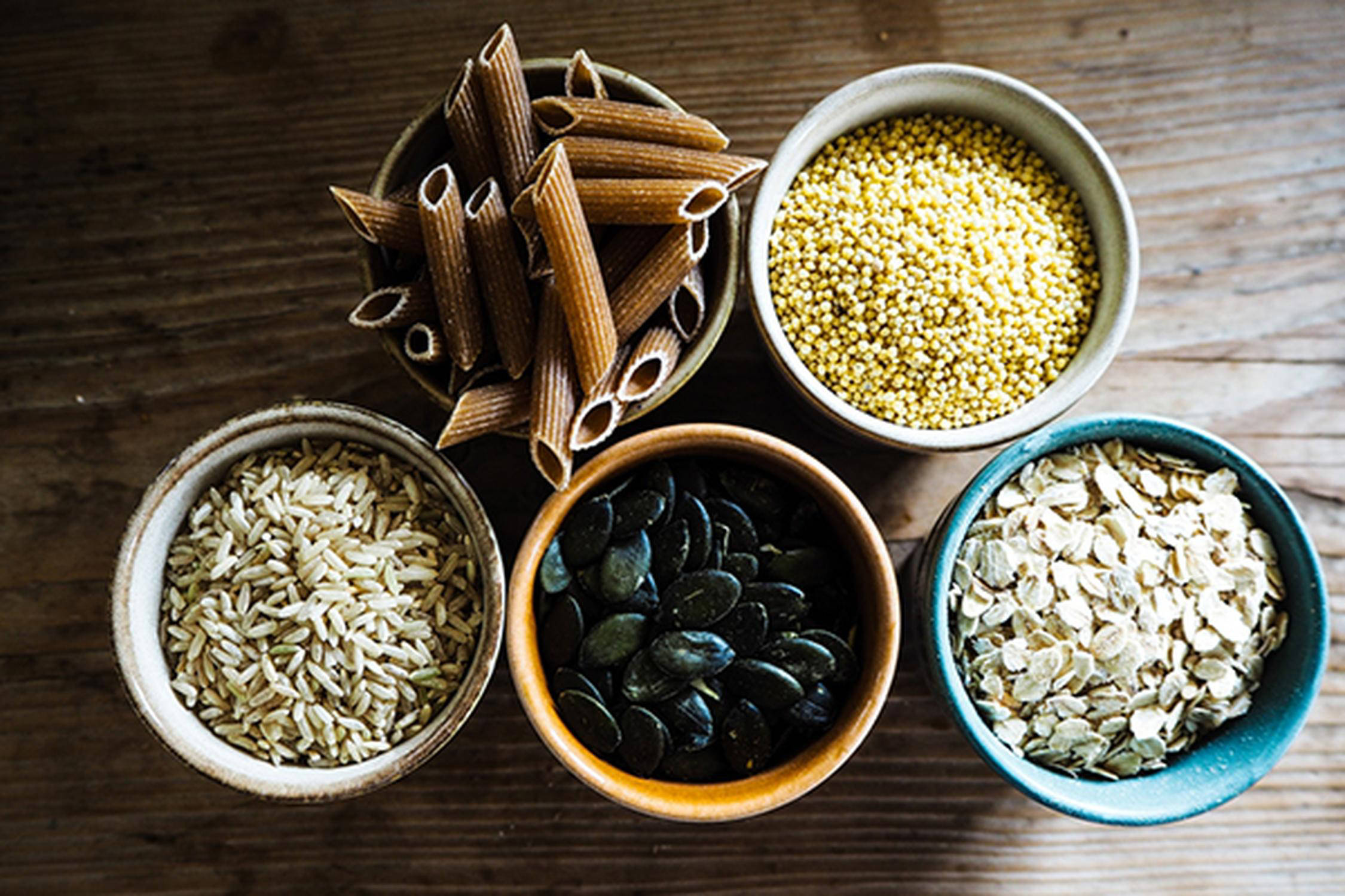 fünf kleine Schüsseln mit Penne, Reis, Kürbiskernen, Haferflocken und Quinoa