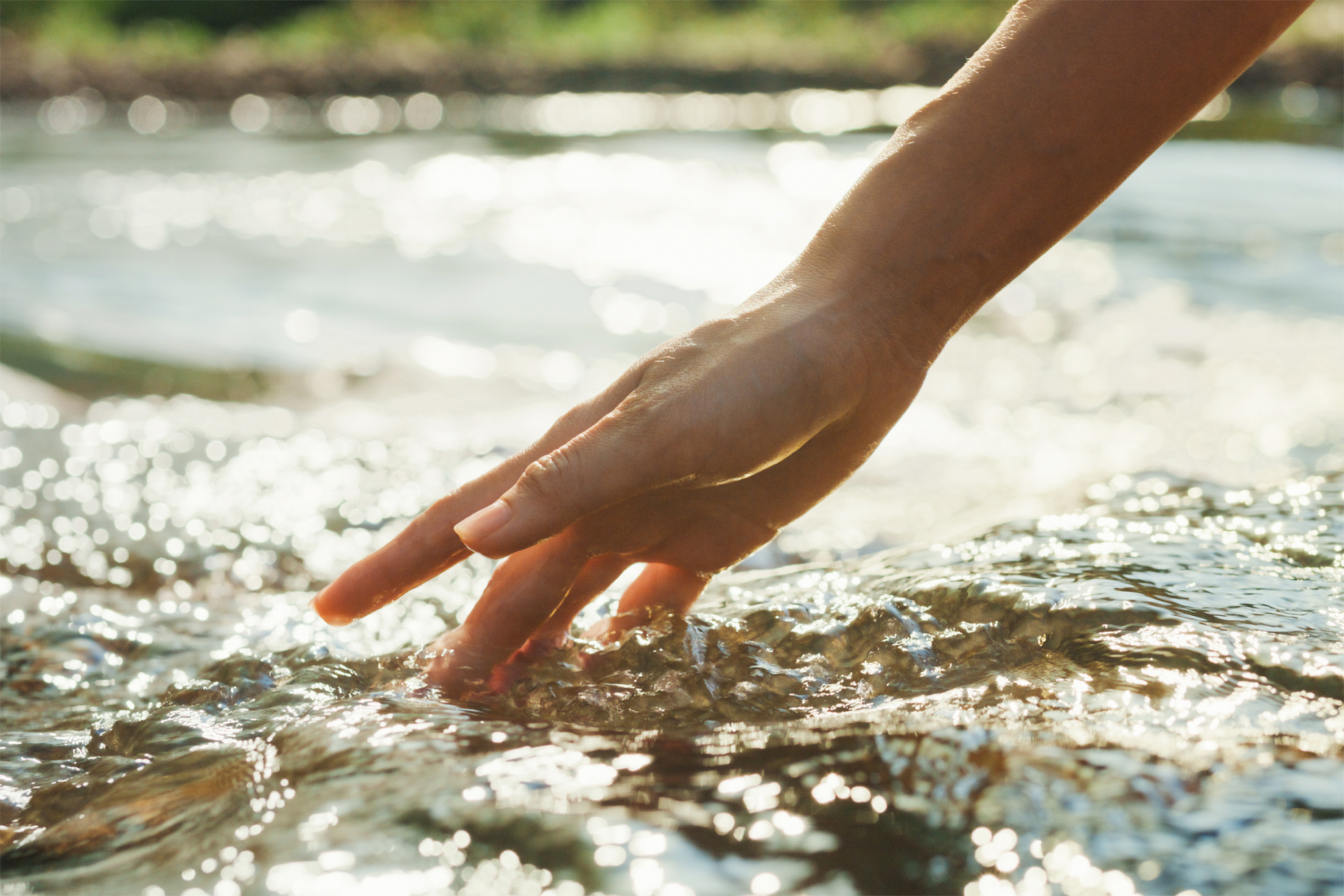 Ein Hand streift durch das Wasser eins Bachlaufs.